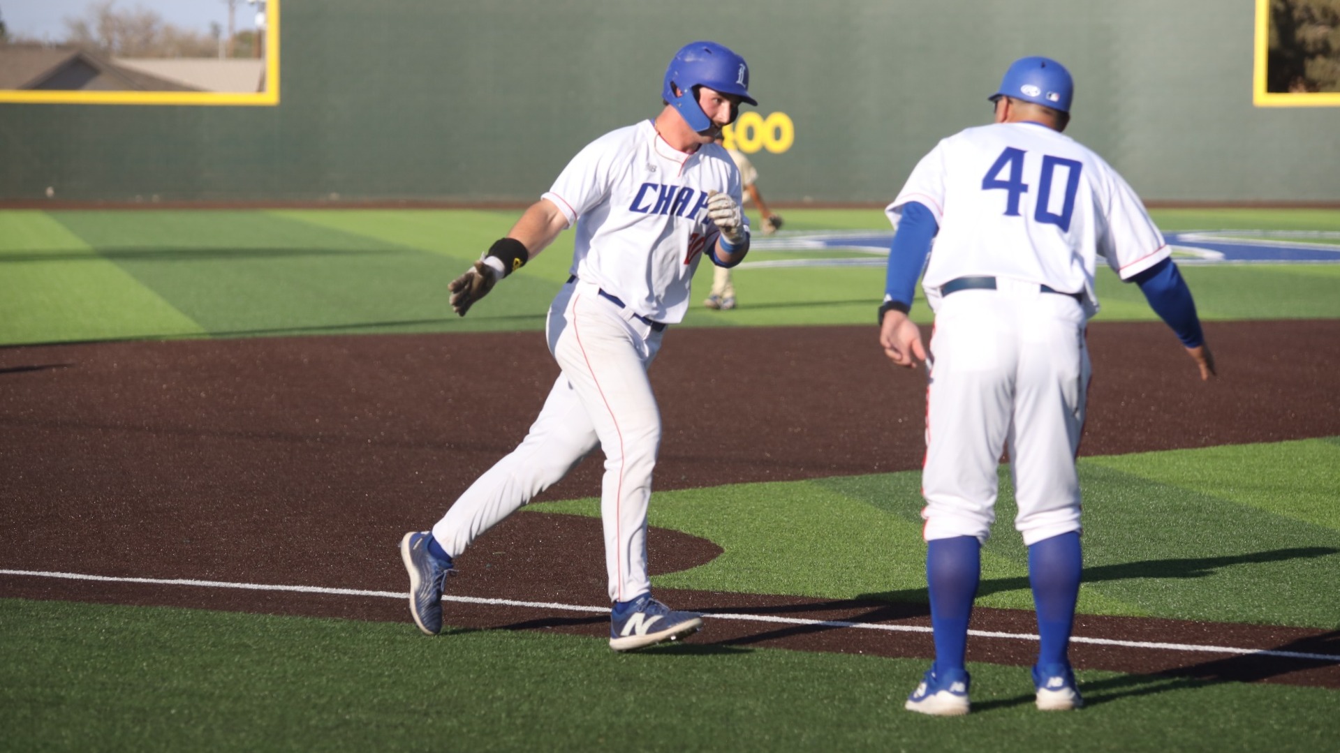 This is a photo of Lubbock Christian outfielder Roe Forrest (white jersey, #20) preparing to high five coach Brandon Walker (white jersey, #40) as he rounds the bases after hitting a home run at Hays Field. 