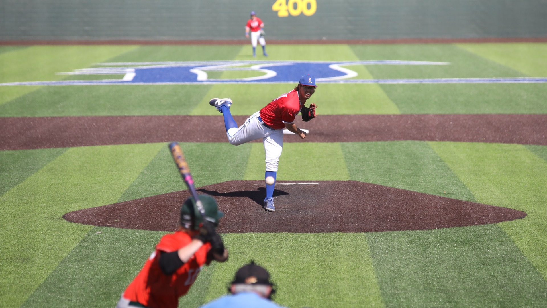 This is a photo of Lubbock Christian pitcher Dakota McCaskill (red jersey, #34) throwing a pitch to a UT Dallas batter (orange jersey) at Hays Field.