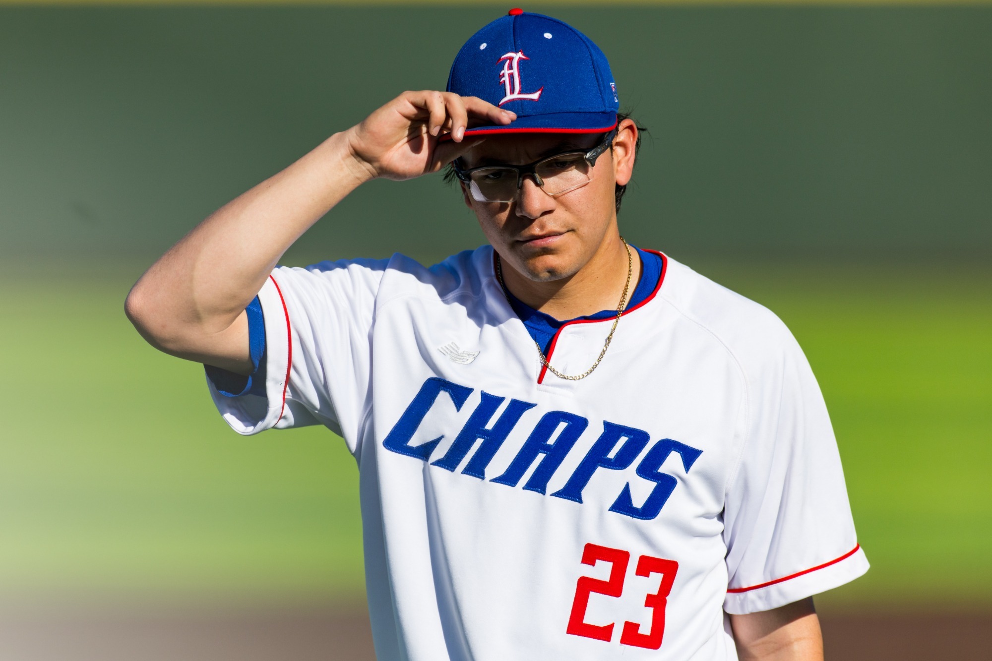 This is a photo of Lubbock Christian pitcher Aaron Rubio (white jersey, #23) touching the brim of his blue baseball cap during a game.