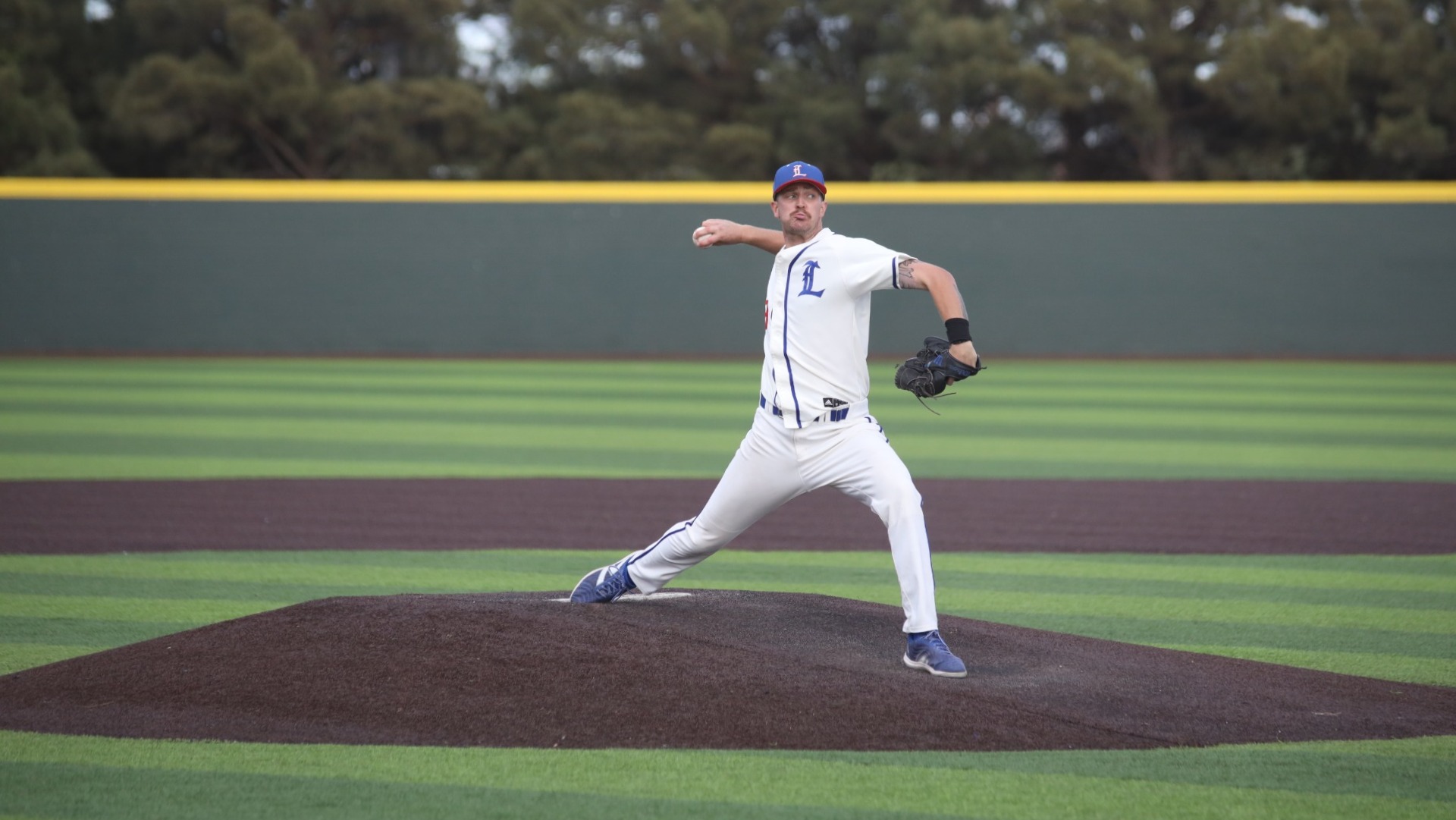 This is a photo of Lubbock Christian pitcher Caden Cline (white jersey, #28) throwing a pitch during a game at Hays Field. 