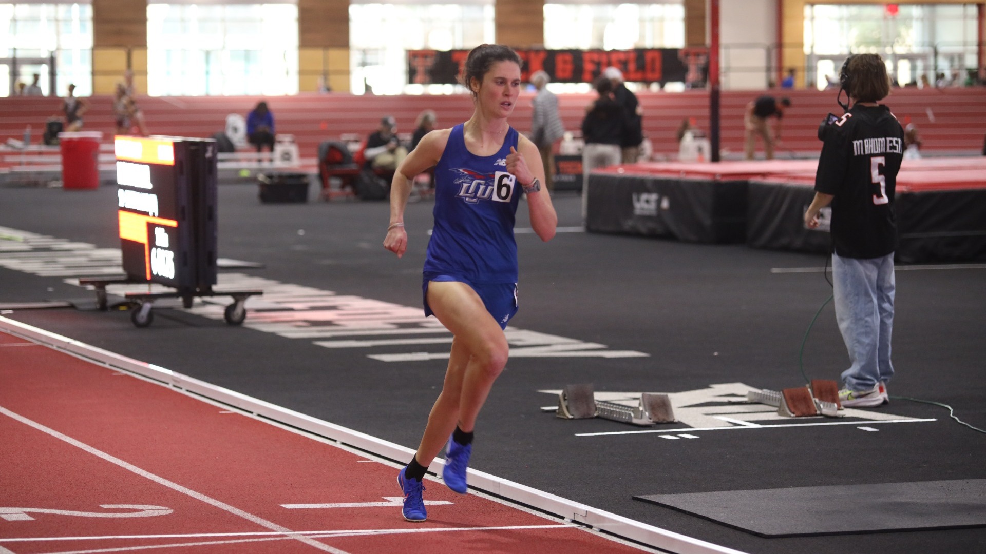 This is a photo of Lubbock Christian track athlete Olivia Weider (blue uniform) running on a red track at a meet hosted by Texas Tech. 