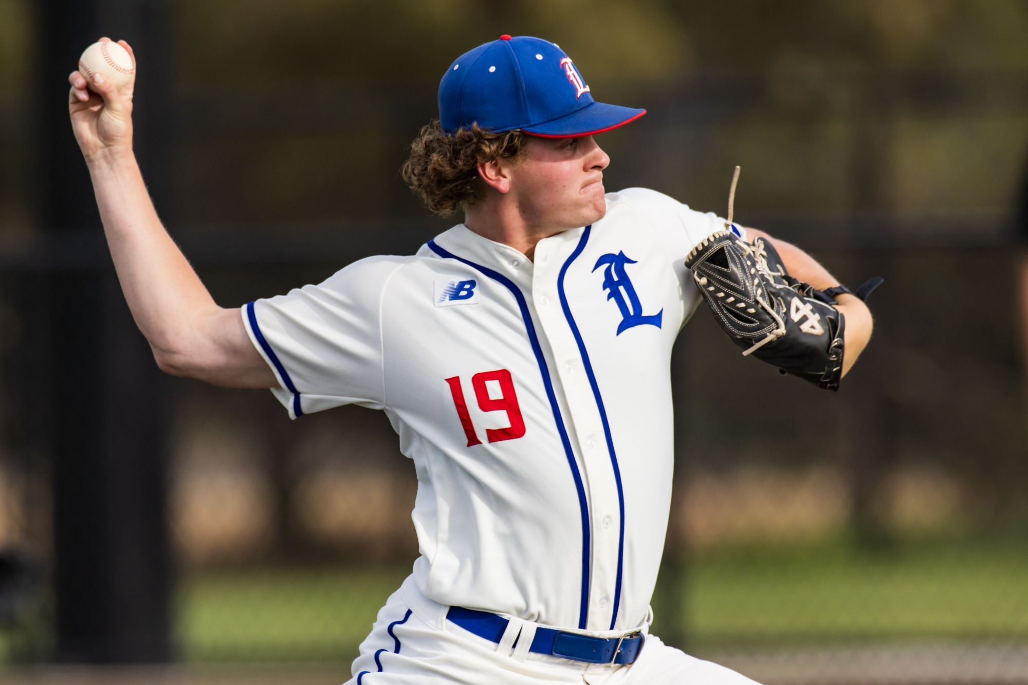 This is a photo of Lubbock Christian pitcher Karson Dunn (white jersey, #19, blue hat) throwing a baseball during a game at Hays Field. 