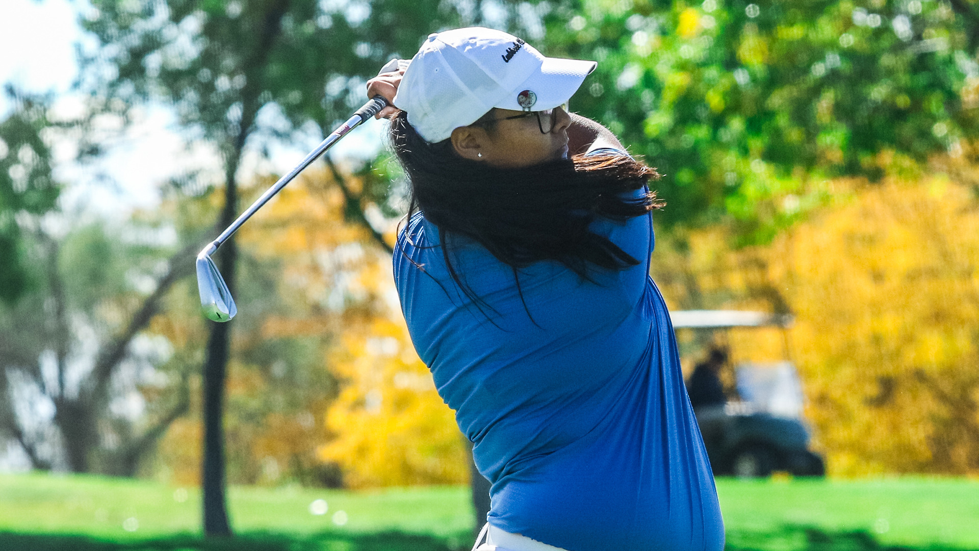 Waist-view and up of a female golpher wearing a blue shirt and focusing on a hit ball...