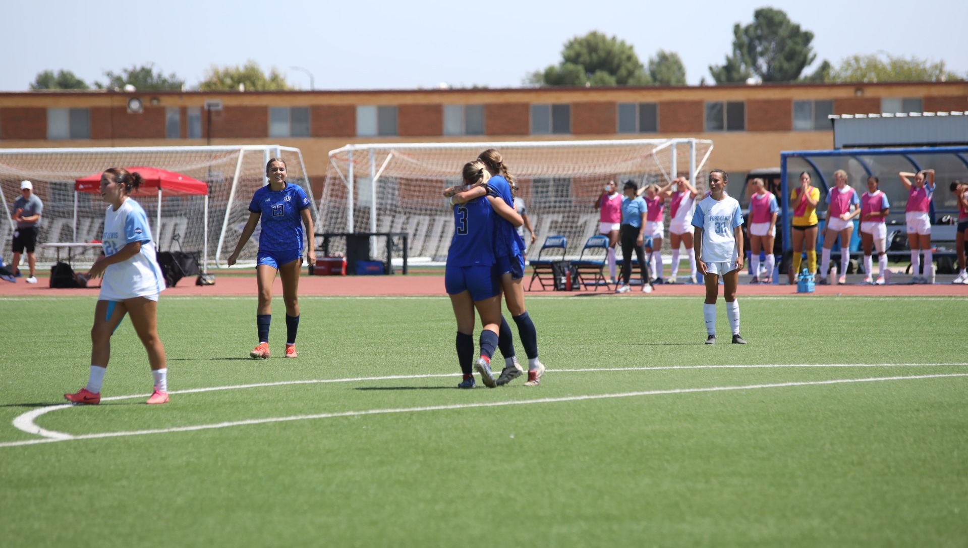 This is a photo of LCU women's soccer player Logan Holloway (blue jersey, #3) hugging a teammate and celebrating after scoring a goal at the LCU Soccer & Track Complex.