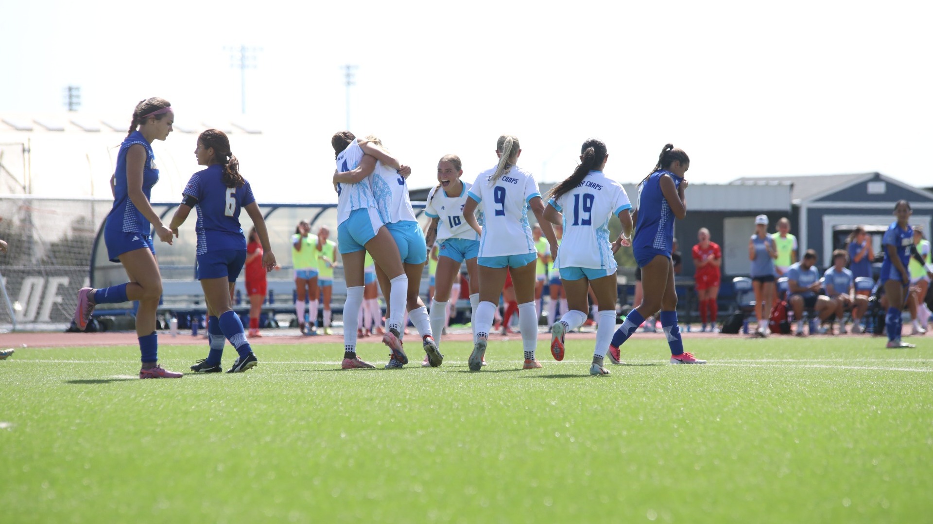 This is a photo of Lubbock Christian women's soccer players (white jerseys) celebrating in the middle of Angelo State players (wearing blue) after a goal at the LCU Soccer & Track Complex.