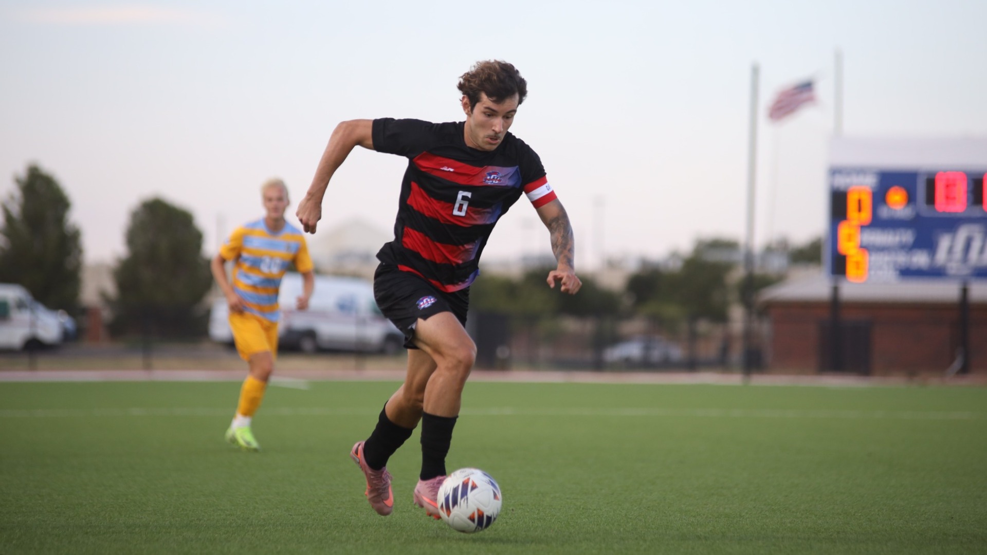 This is a photo of midfielder Joao Catafesta (black jersey, #6) dribbling the soccer ball up the field during a game at the LCU Soccer & Track Complex. 