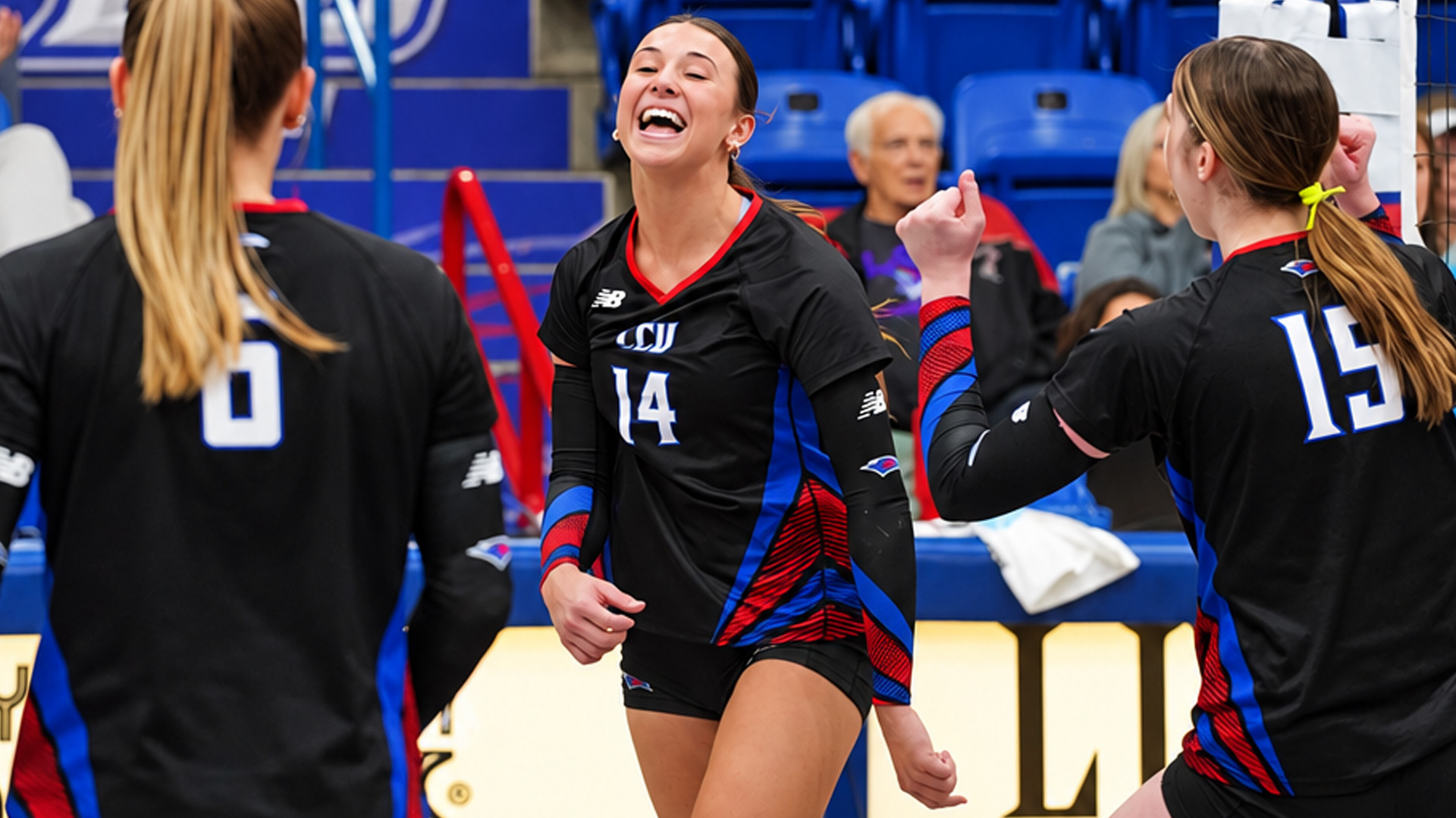 Celebratory photo of LCU volleyball players in black jerseys on the court. Player #14 laughs joyfully in the center, fists clenched, while teammates #6 and #15 stand nearby, one with an arm raised. Blue stadium seating and seated spectators are visible in the background.