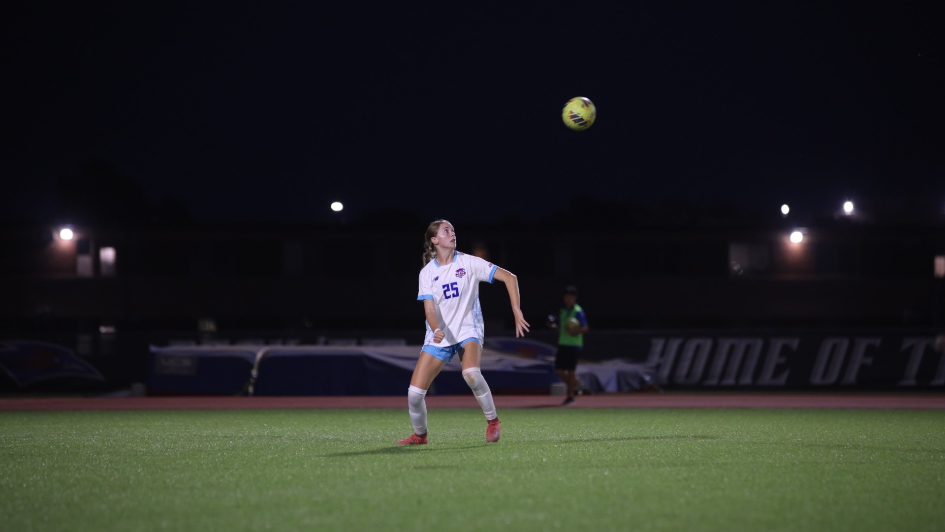 This is a photo of Lubbock Christian women's soccer player Trinity Doom (white jersey, #25) preparing to head a yellow soccer ball in a game at the LCU Soccer & Track Complex.