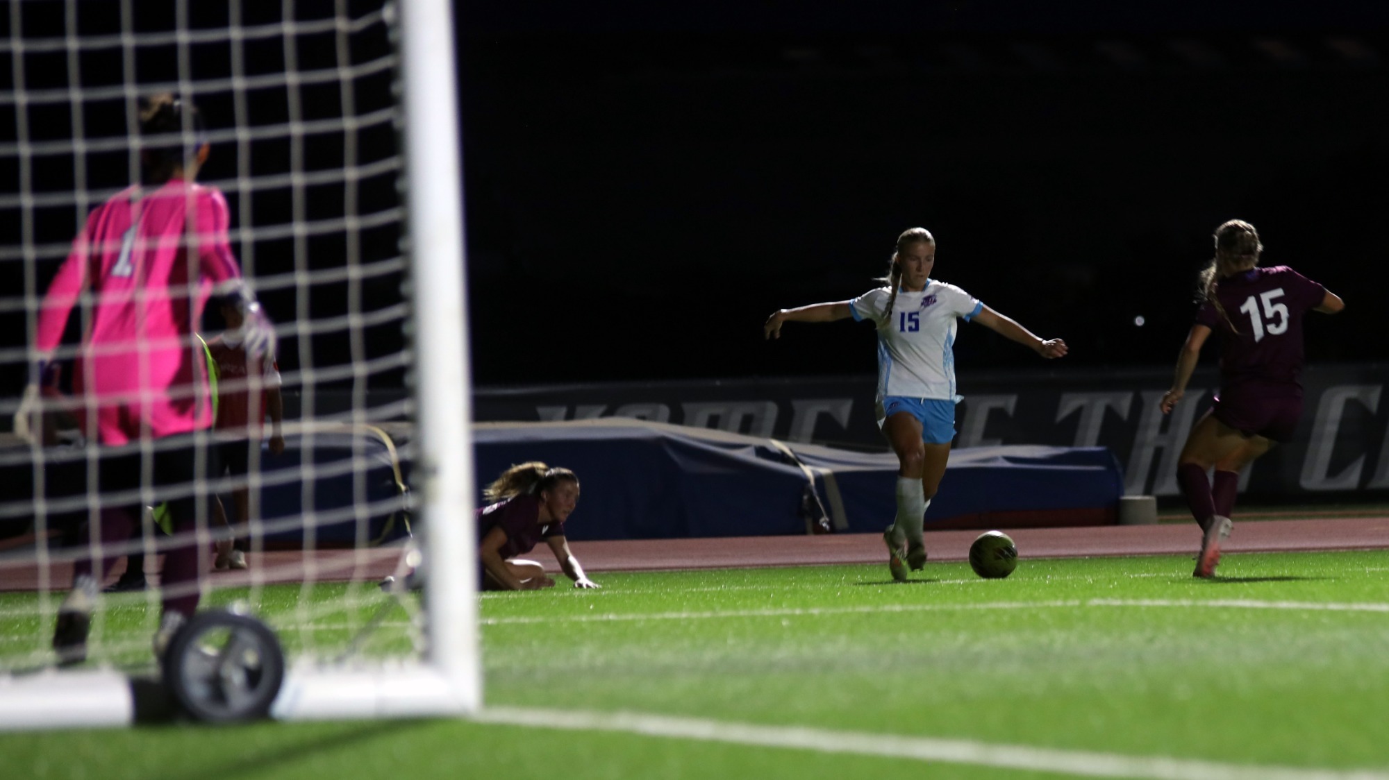 This is a photo of Lubbock Christian forward Kaslee Roskelley (white jersey, #15) preparing to kick a ball into the box during a game at the LCU Soccer & Track Complex. 