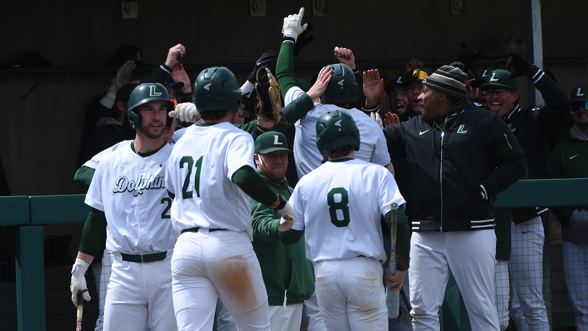 The baseball team celebrates a run at the dugout