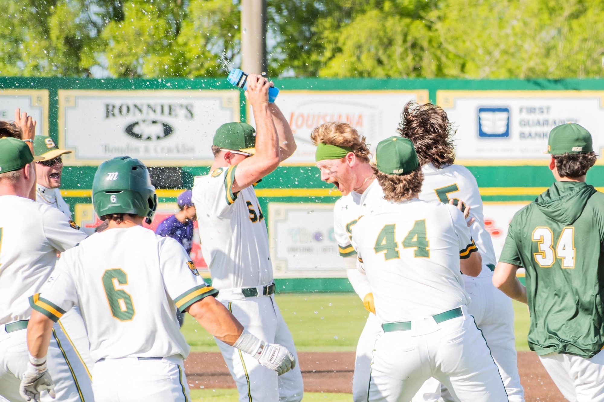 Blaise Priester, wearing a green bandana, gets sprayed with water as he celebrates his game-winning hit with his teammates. 