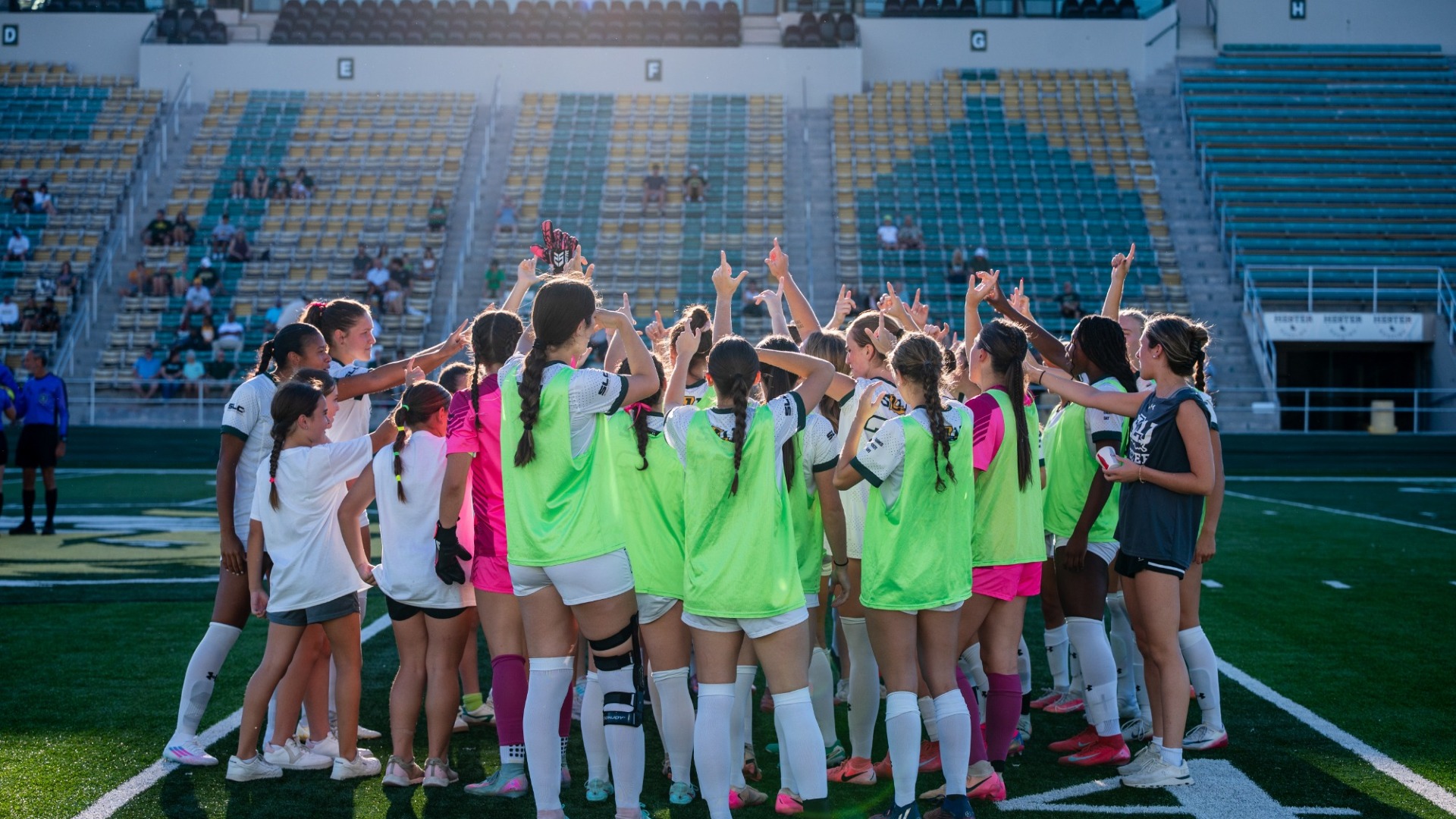 Women's soccer student-athletes gather around in team huddle before match, getting ready for warmups