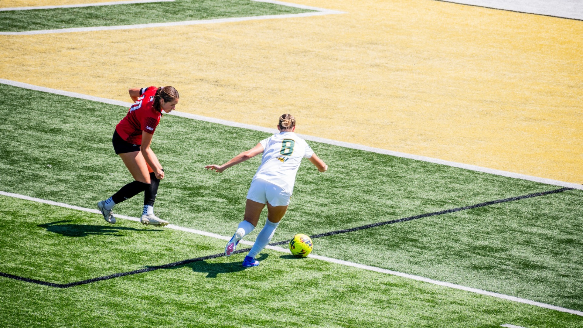Brooke Opferman (white jersey) gaining control of the ball vs UIW defender (red/black jersey) at home in Strawberry Stadium
