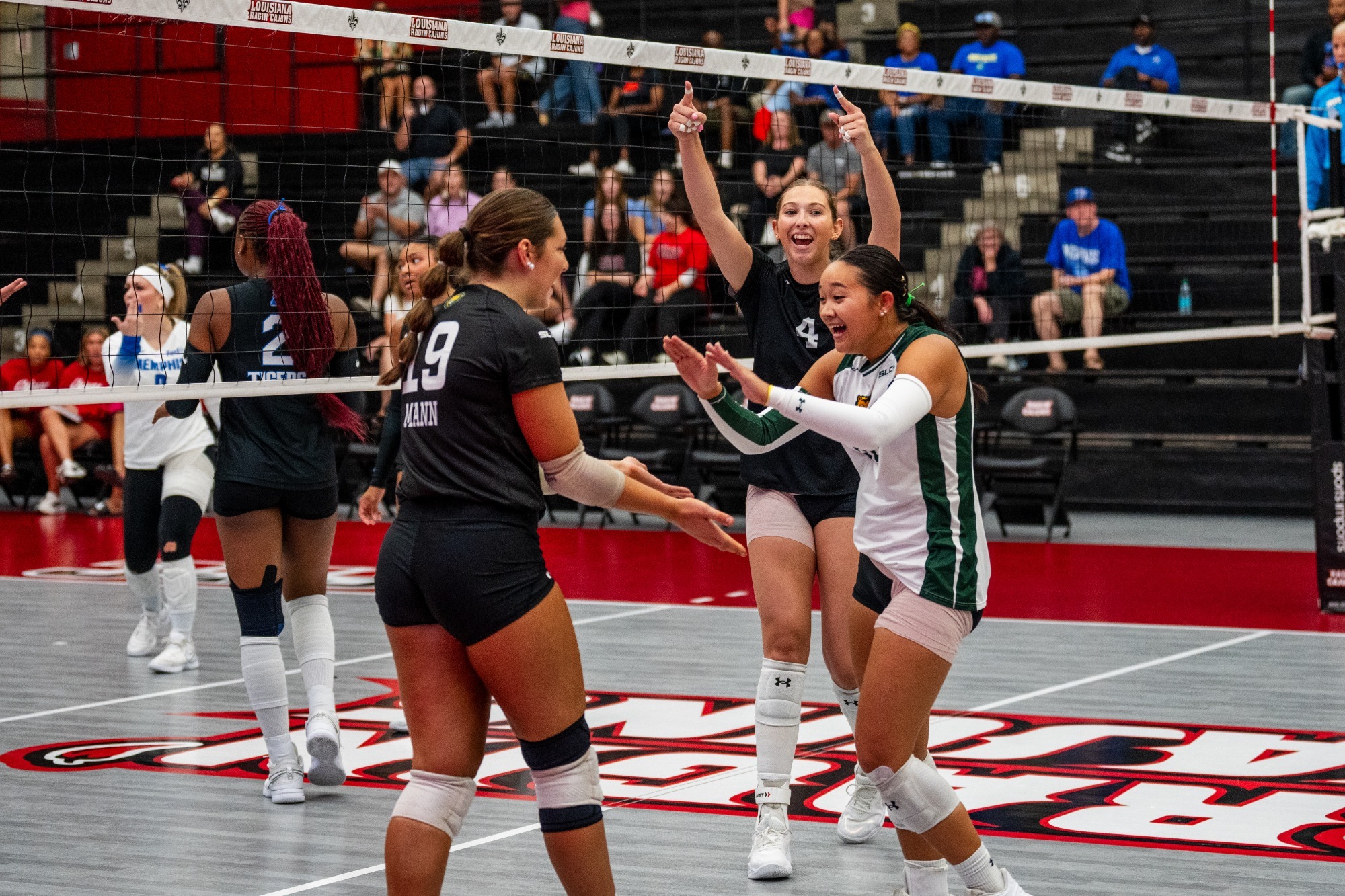 Gracie Mann, Audrey Vielguth, and Ainsley Driska celebrate after a point in at E.K. Long Gym in Lafayette, La. 