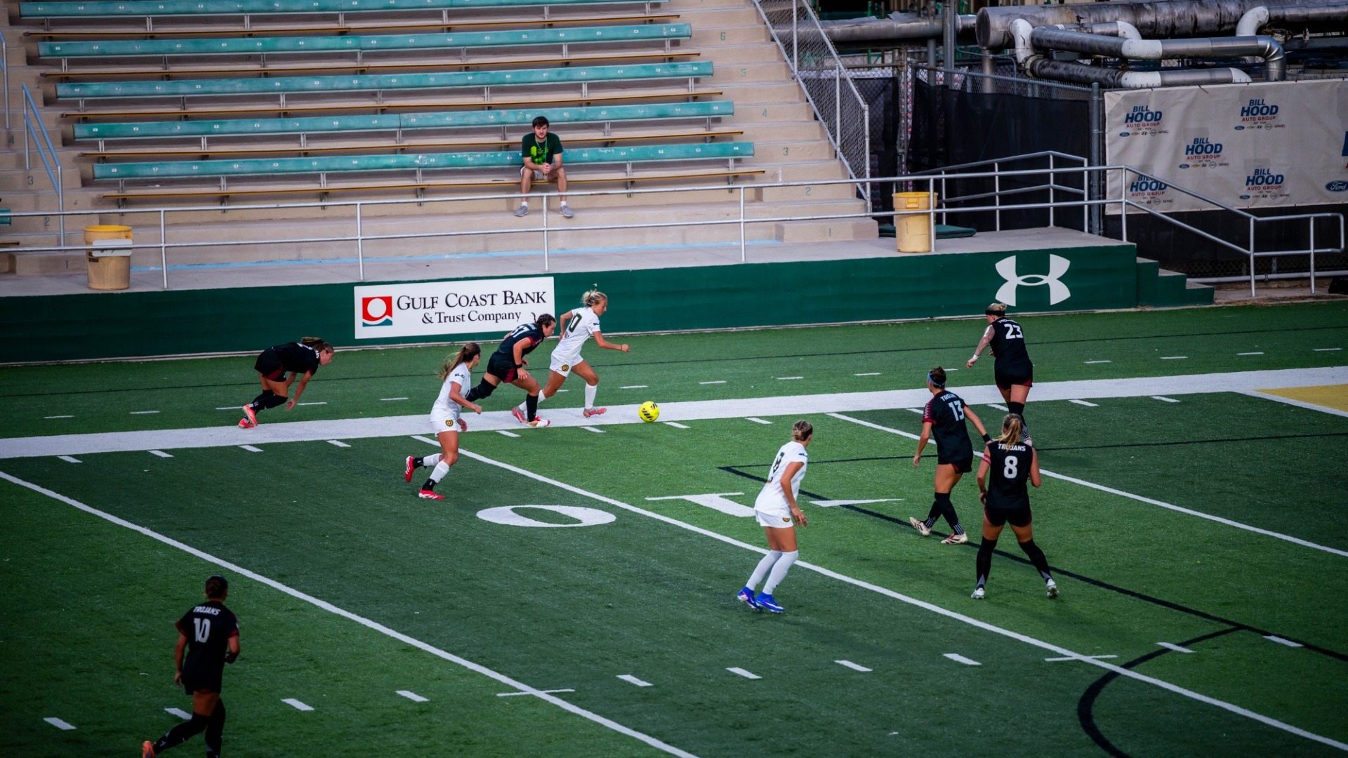 Women's soccer player Kaitlyn Tung working to push the ball up the field vs multiple Troy defenders in black jerseys 