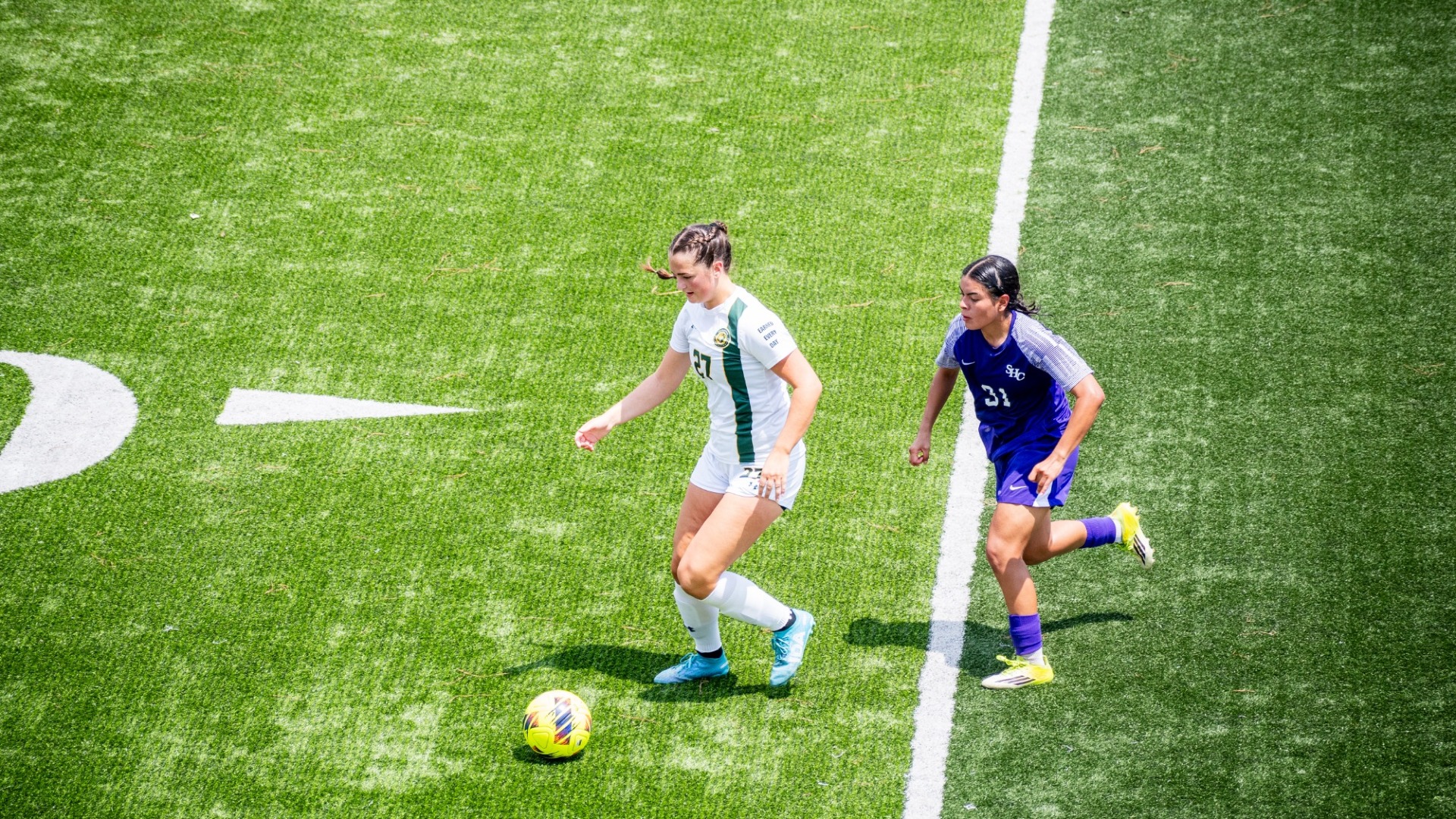 Women's soccer player (in a white jersey) Madison Vogler working to evade a Spring Hill defender (in a purple jersey) to keep the ball for an offensive attack