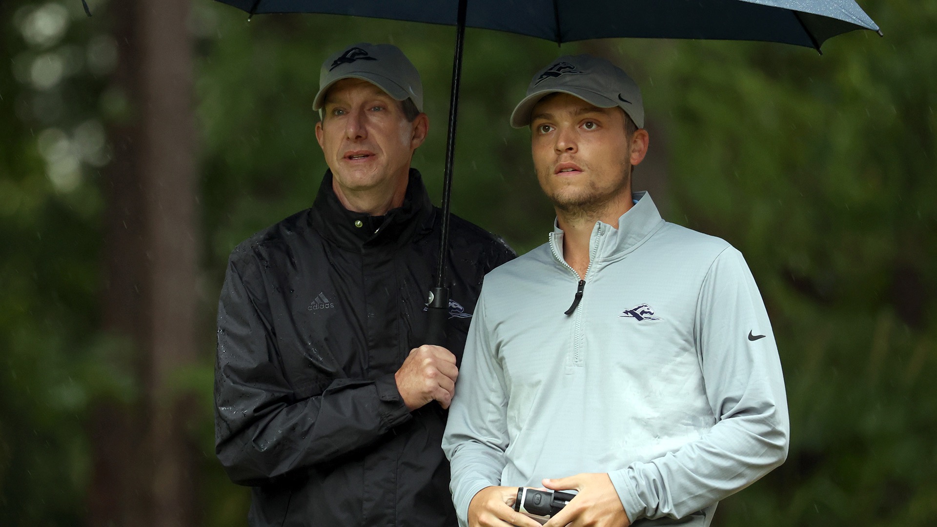 Head coach Kevin Fillman holds an umbrella and discusses a shot with graduate student Nick Fleming on the tee box during play at the NC State Intercollegiate in 2024. 