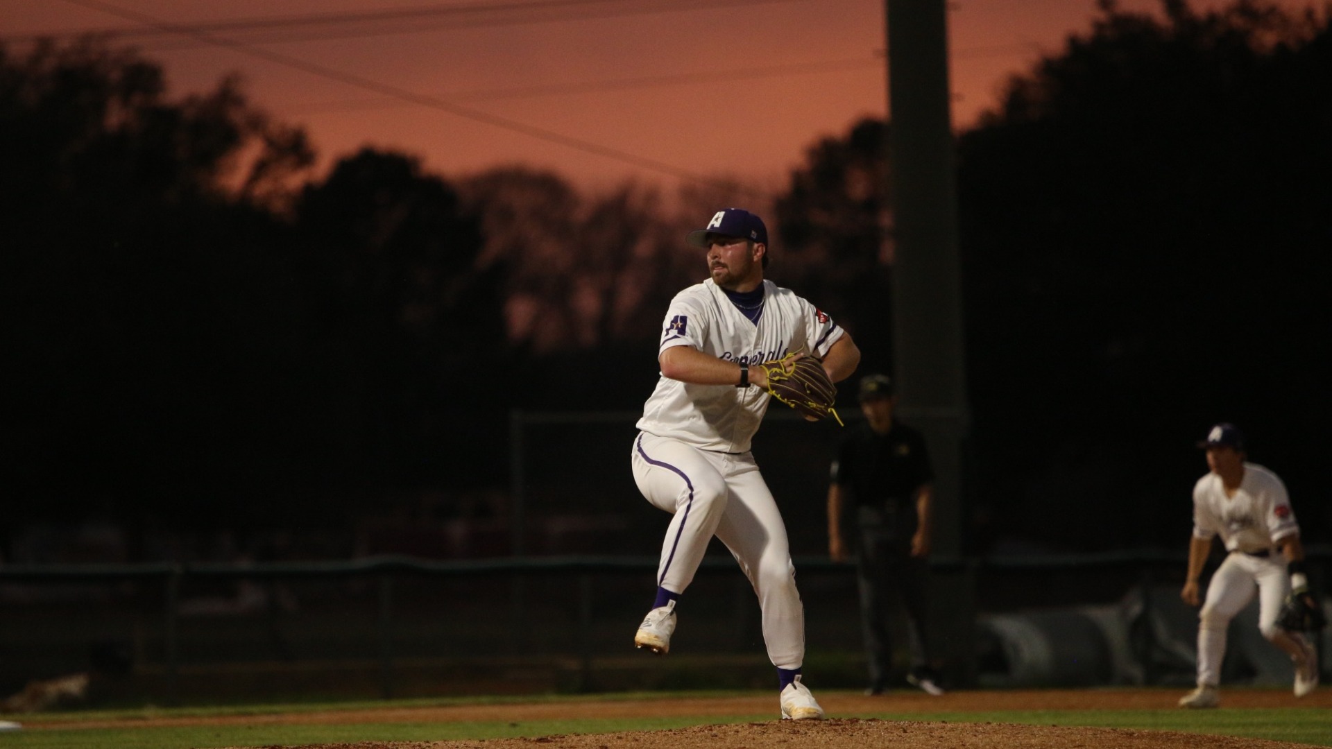 Michael Sutton delivers a pitch against LSUS with a pink sunset sky behind him