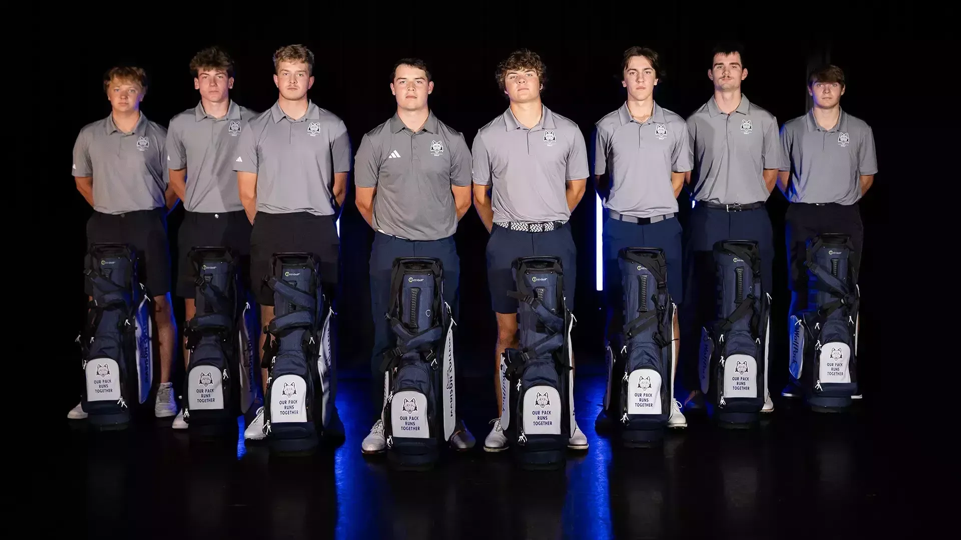 The golf team stands behind their golf bags in a 