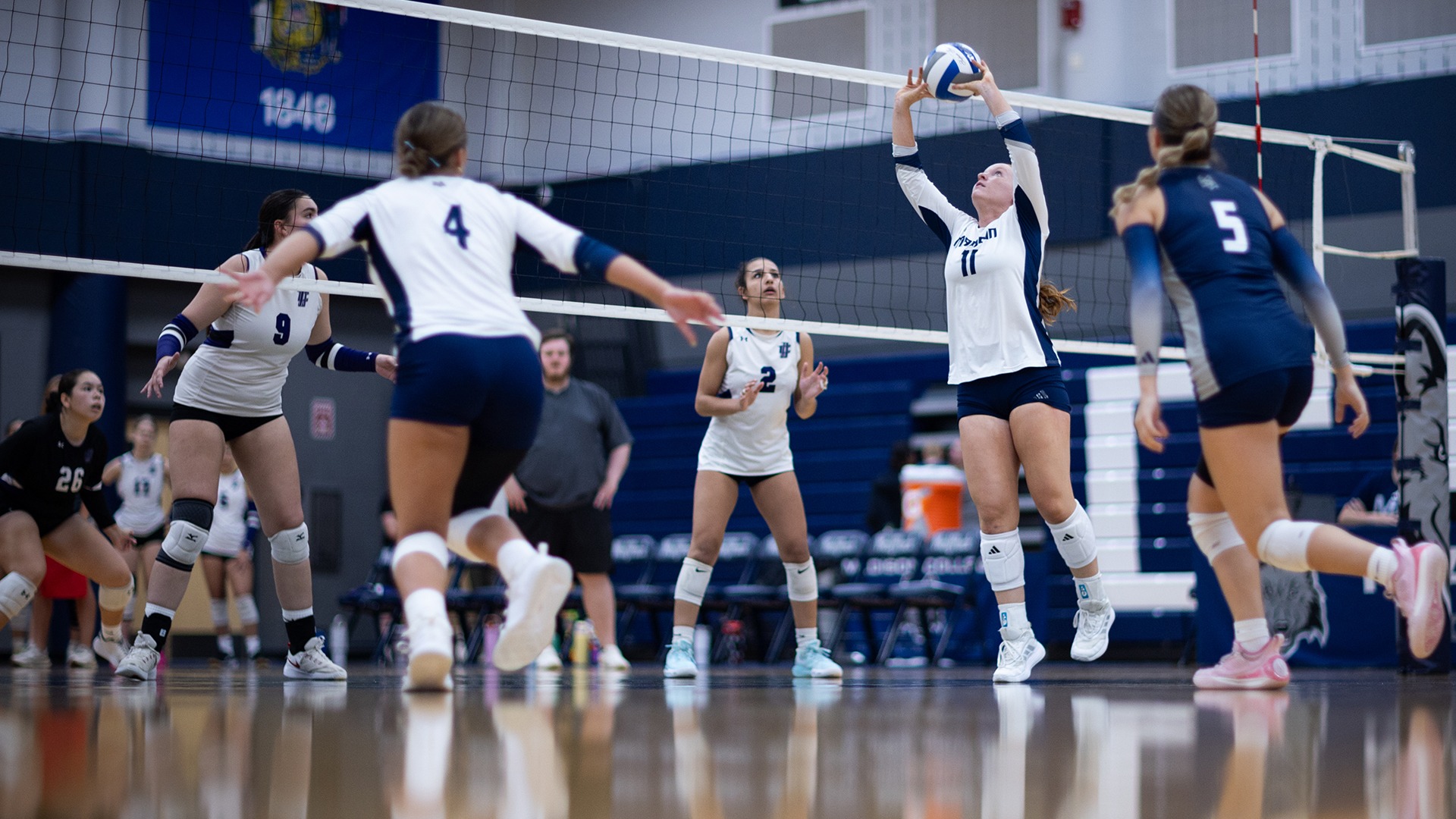 Allie Andrews sets a volleyball for teammate Makayla Dallas as libero Jaydon Golsteyn and opponents look on.