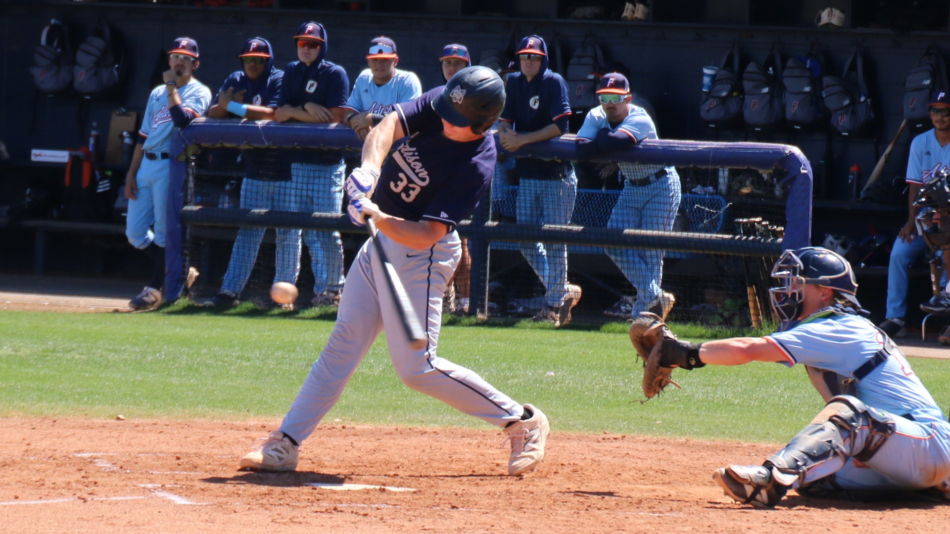 Ian Salvesen swings from the left side of home plate at an on-coming pitch as the opposing catcher waits with glove ready.