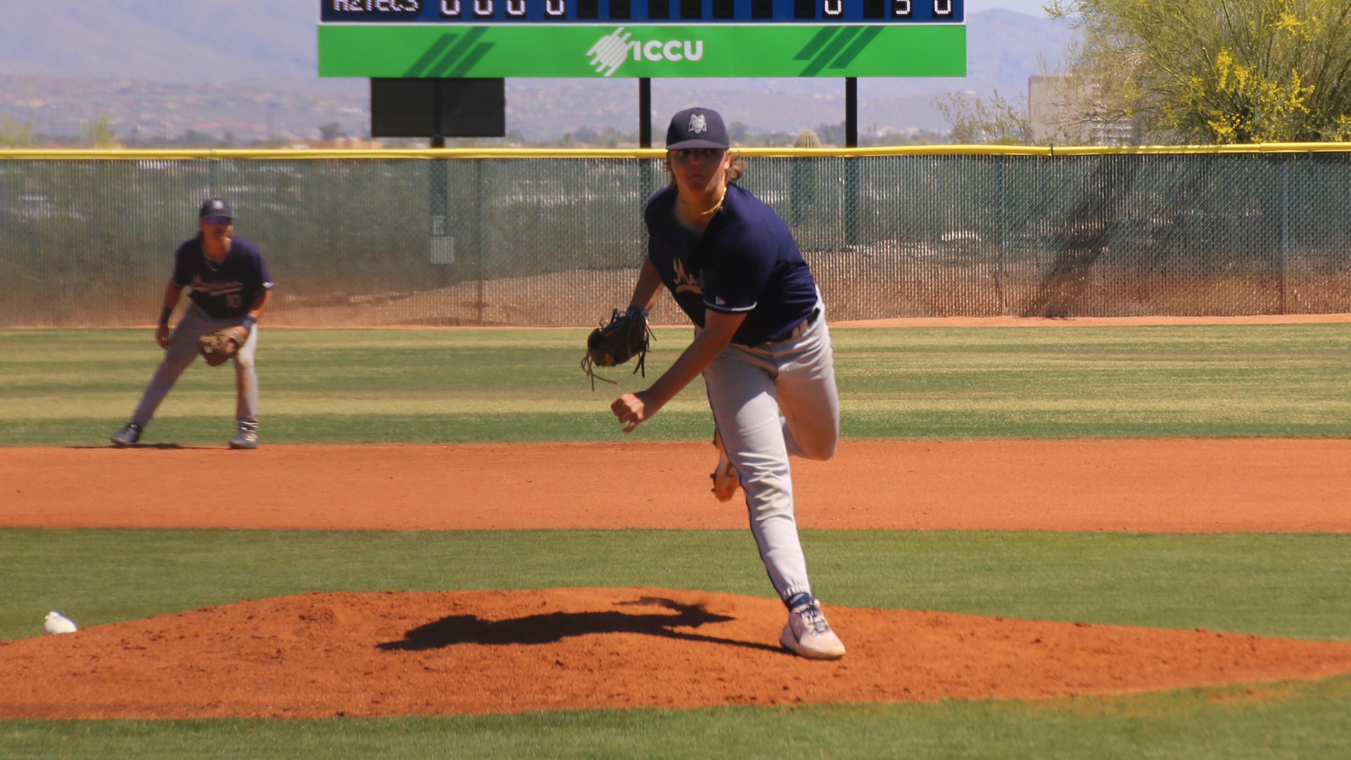 Lefthanded pitcher Aaron Ploszay follows through on a pitch atop the mound as second baseman JJ Wolbert watches from behind him.