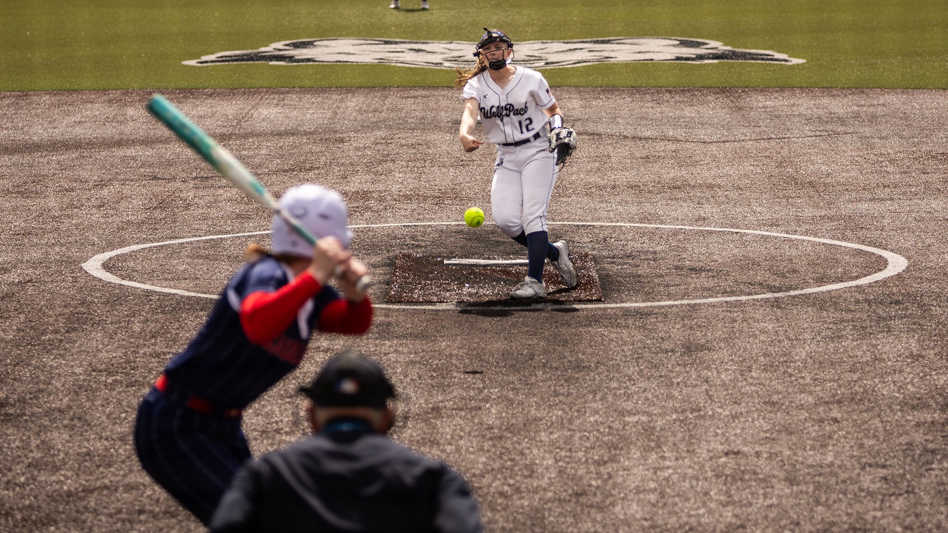 Lauryn Etienne throws a pitch straight at the camera at Robin Roberts Field with the batter and umpire waiting.