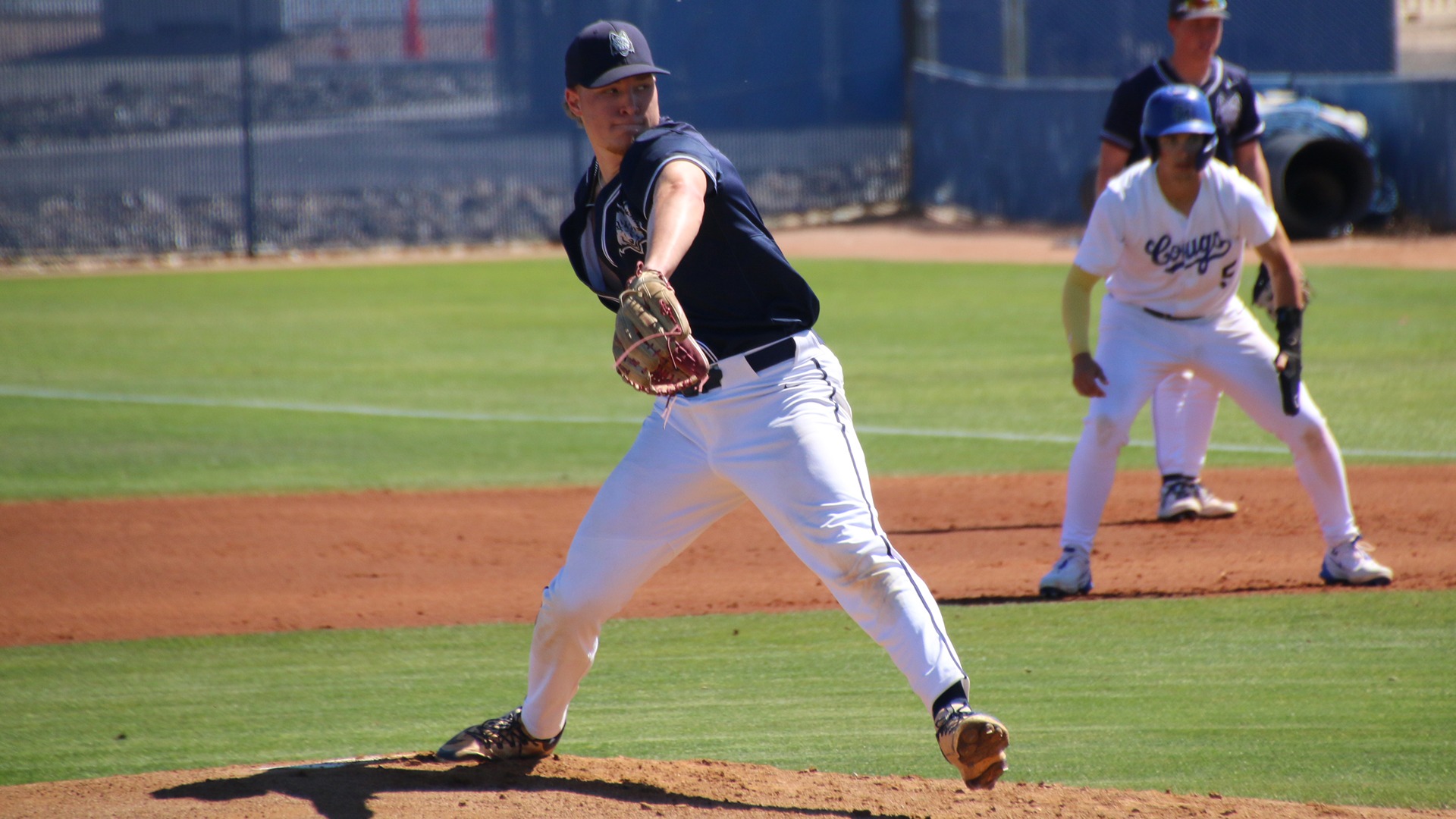 Broden Jackson is in the process of throwing a righthanded pitch with a baserunner and infielder looking on in the background.