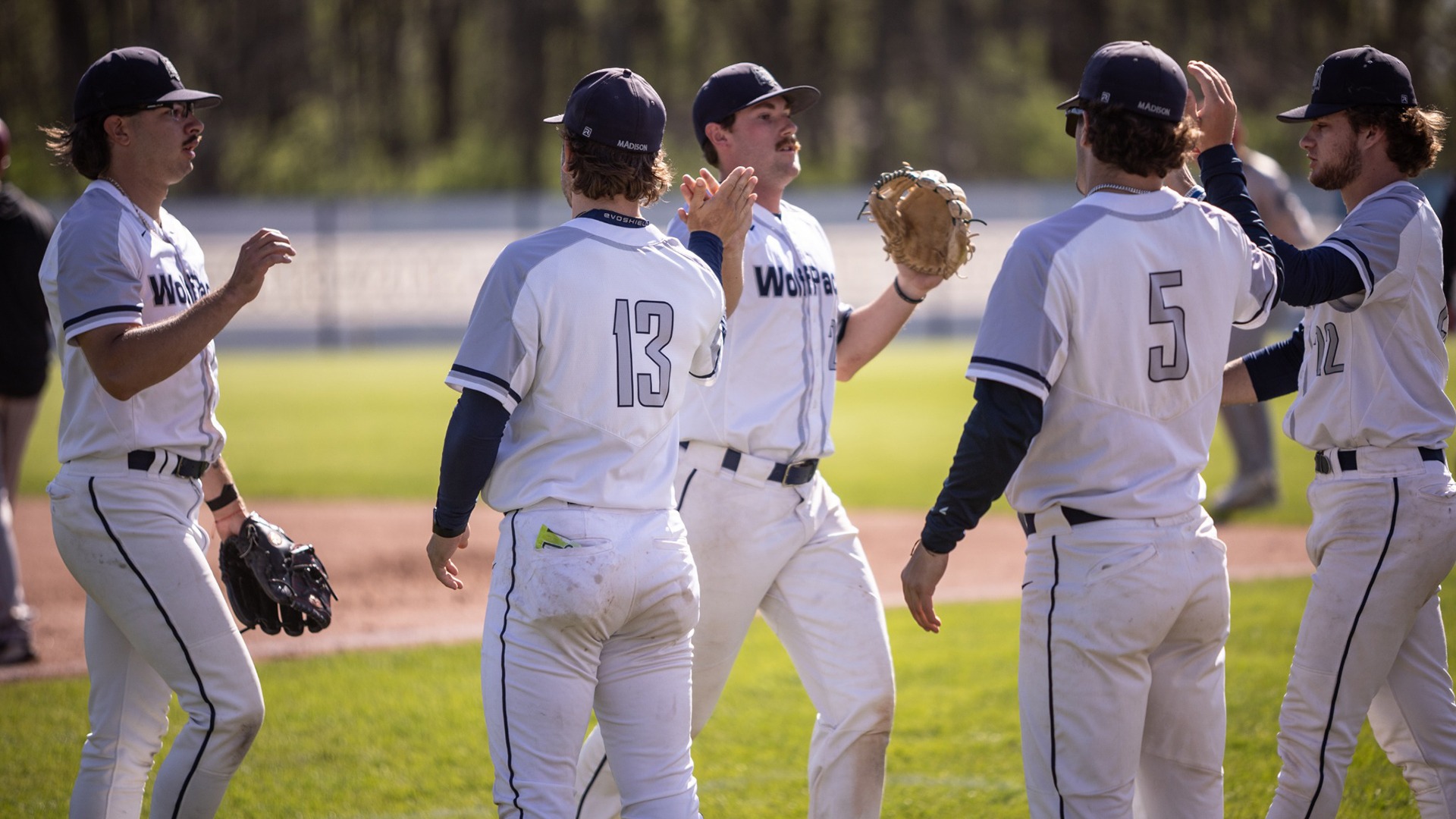 Members of the 2026 baseball team give high fives as they enter the dugout.