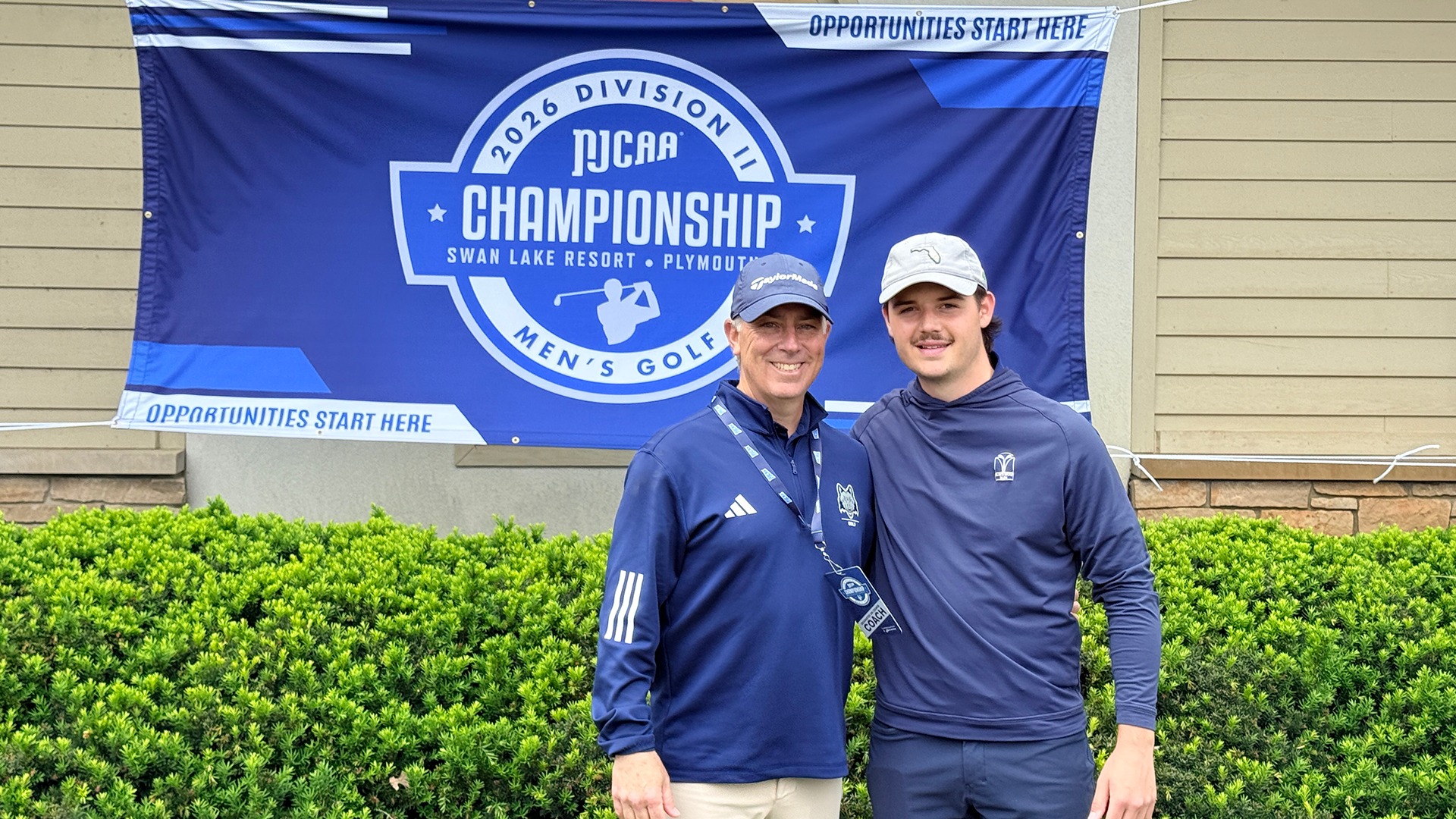 Golfer Matthew Haggart and coach Chris Soulier stand in front of the NJCAA Division II Men's Golf Championship banner in Indiana