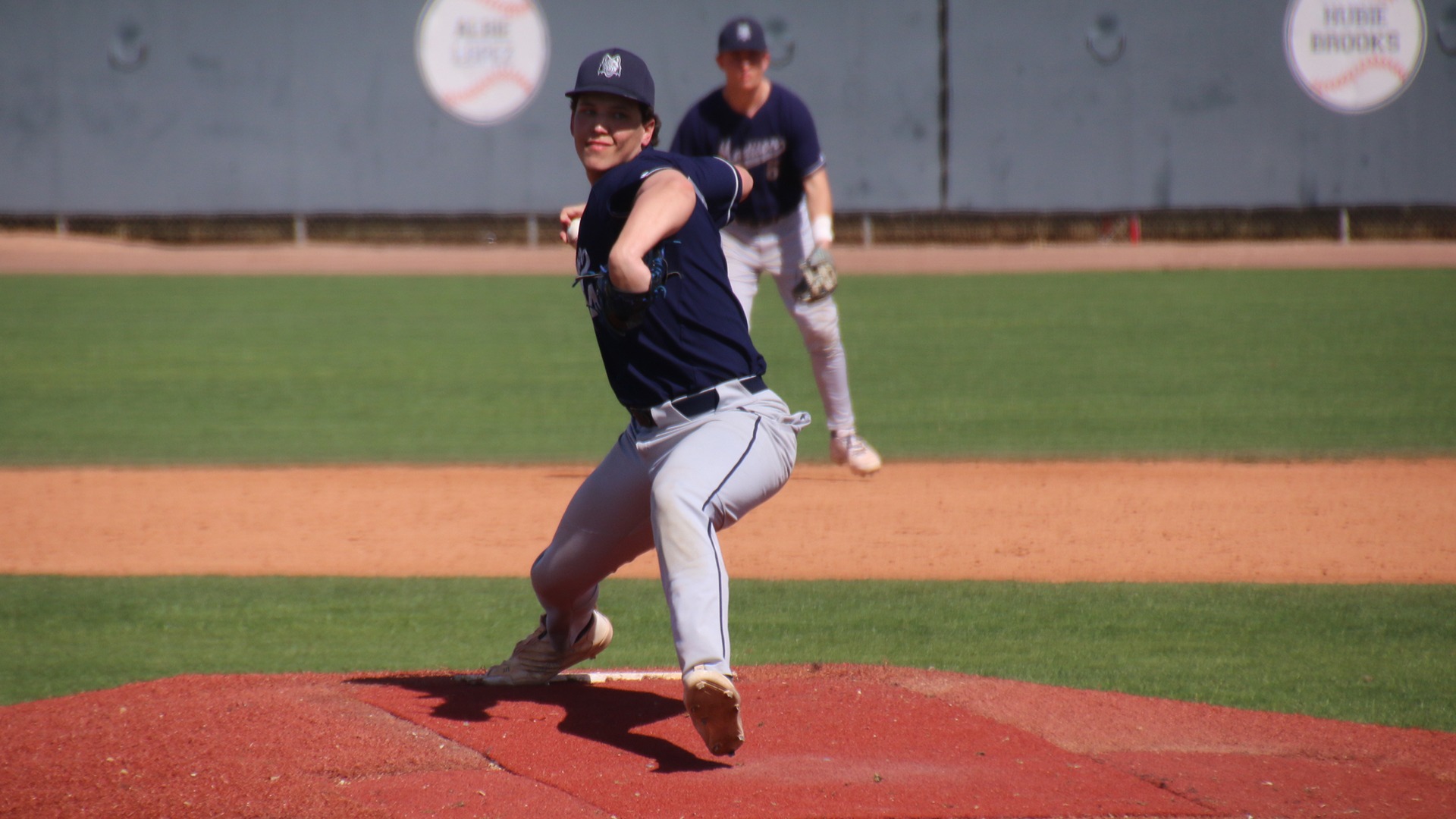 Tavian Shramek throws a pitch as the second baseman looks on from behind.