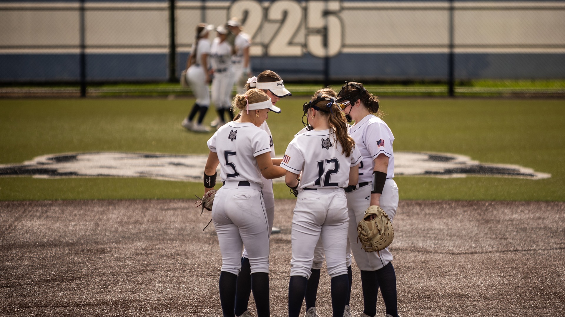 Five softball players huddle in the infield while three more do the same in the outfield.