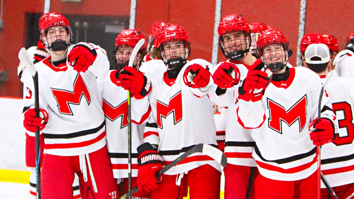 Men's Hockey Players point to the camera while on the ice