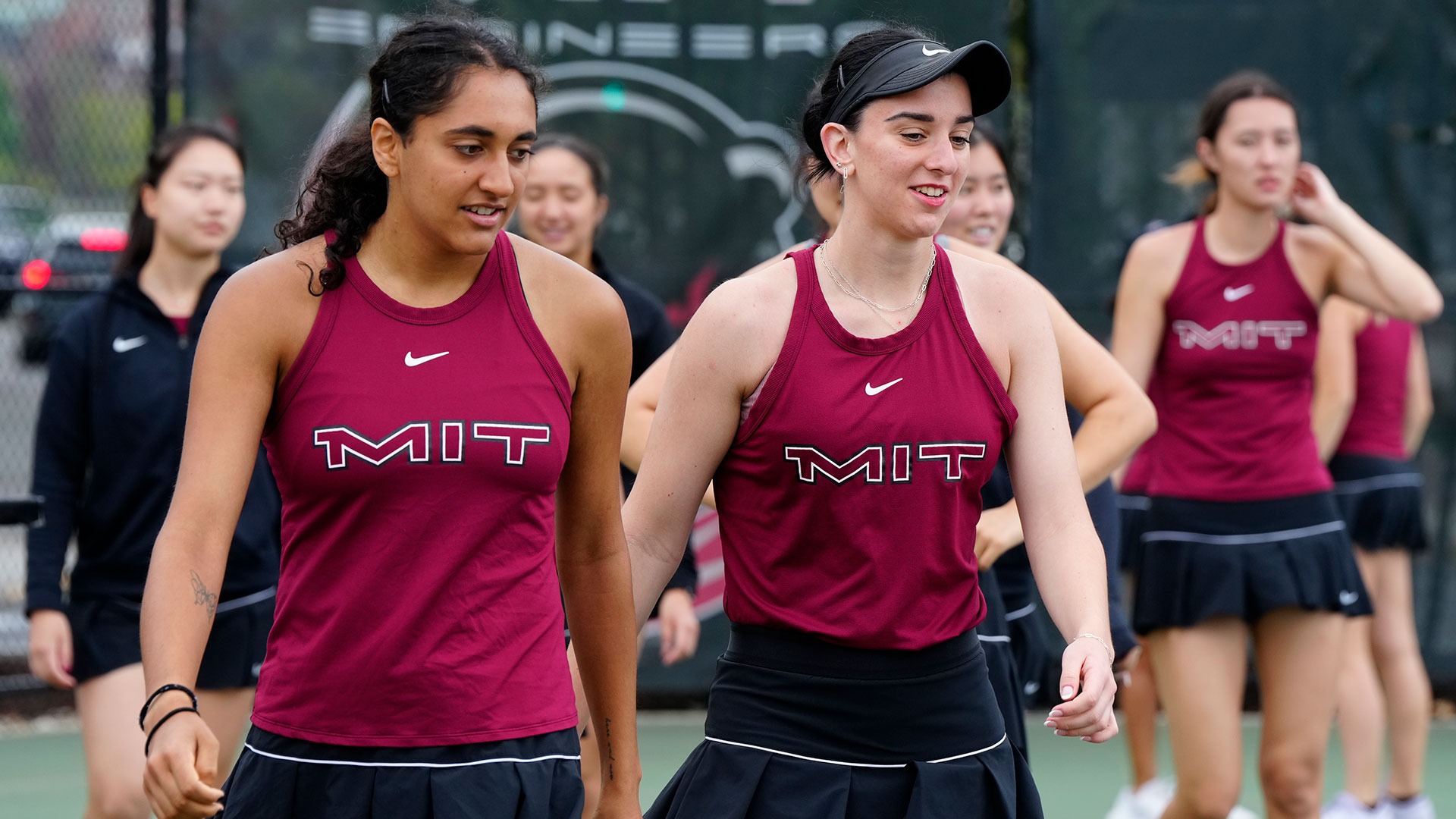 Alaina Kolli and Artemis Pados walking in front of other members of the women's tennis team on the tennis court
