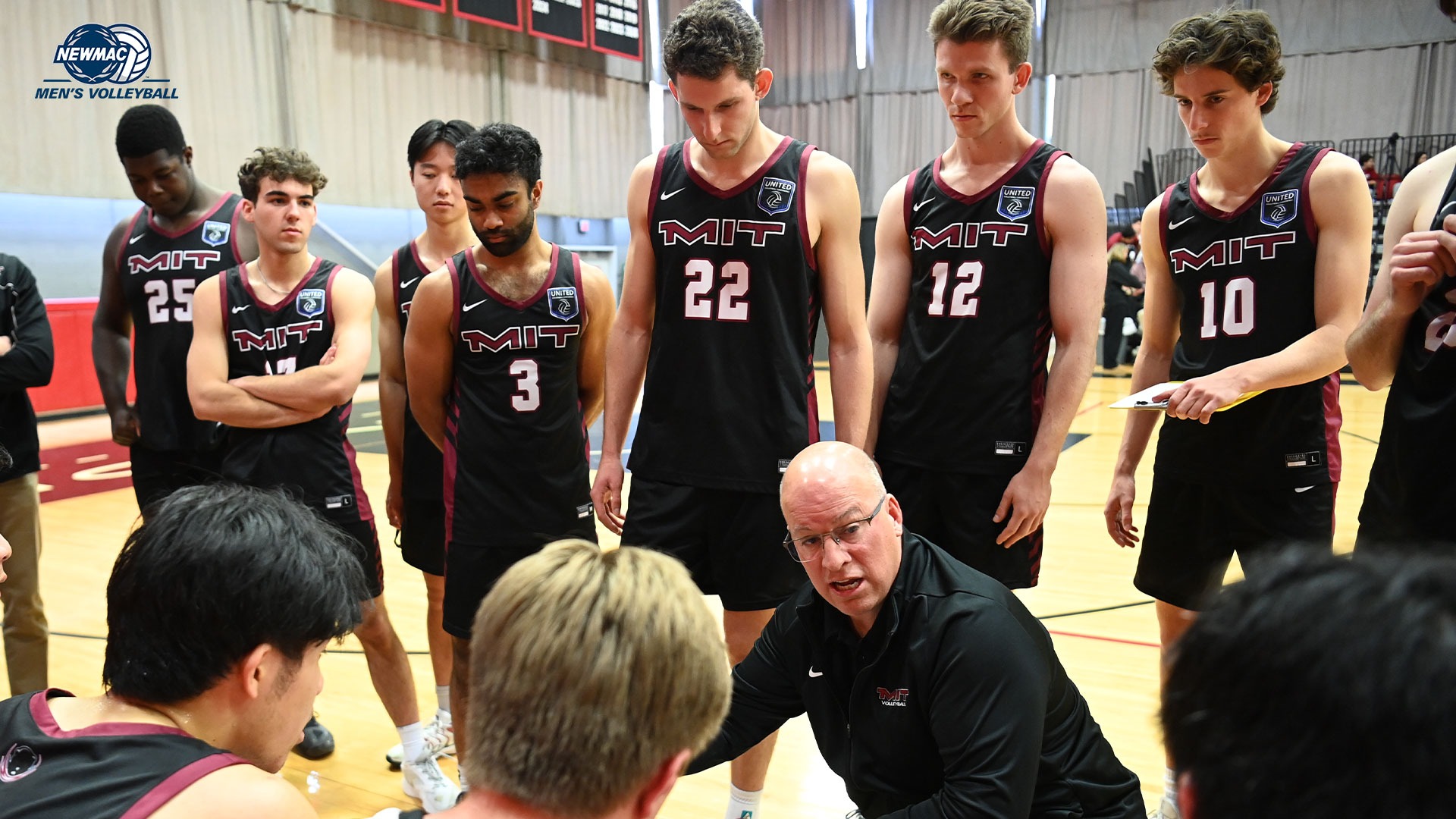 The MIT volleyball team in a huddle on the bench with the NEWMAC Volleyball Logo