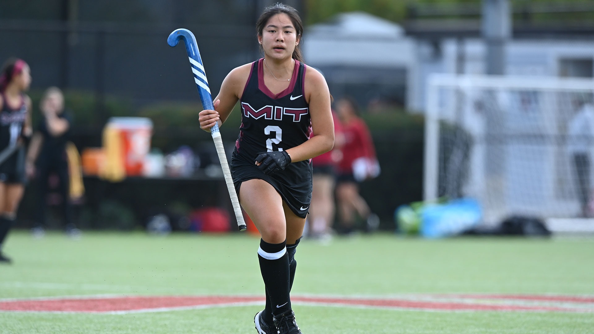 Audrey Oh running down the field holding her field hockey stick