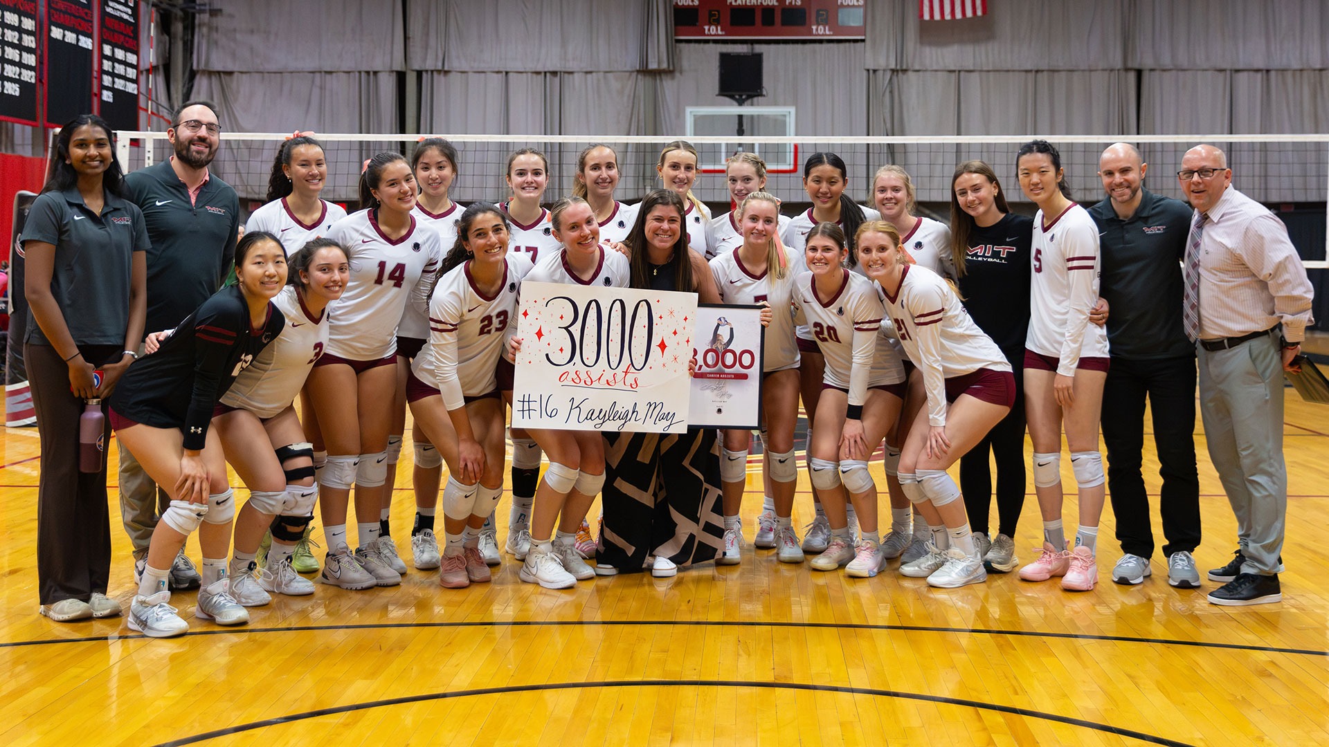 The MIT women's volleyball team with Kayleigh May holding a poster celebrating 3,000 career assists
