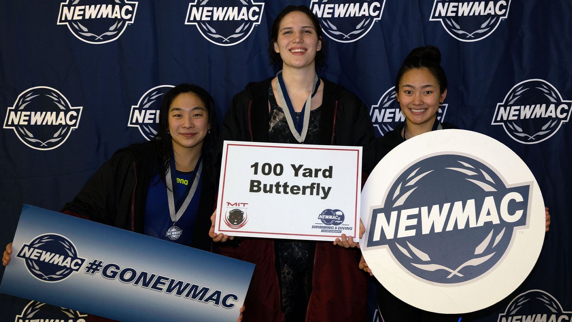 Sydney Smith, Belise Swartwood, and Kathy Nie holding the 100 Fly NEWMAC Sign