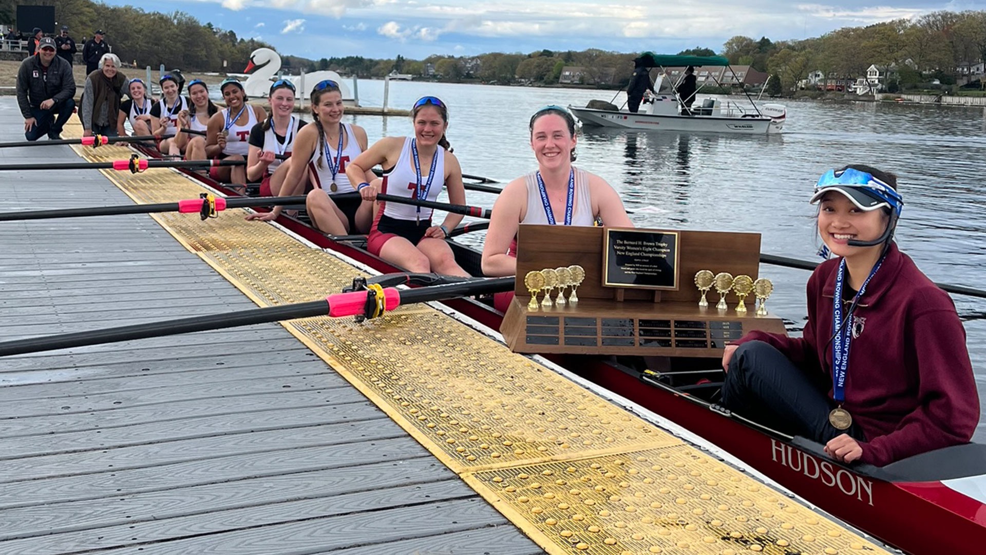 MIT women's openweight varsity eight sitting in a boat with a trophy