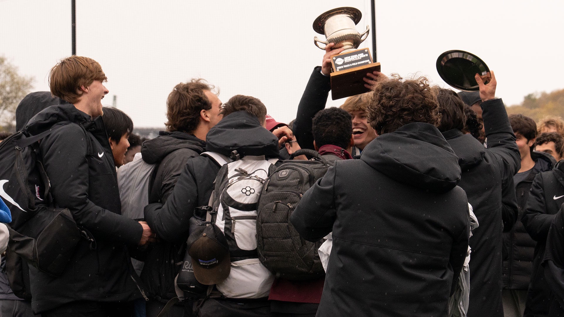 men's track and field celebrates with the NEWMAC Championship trophy