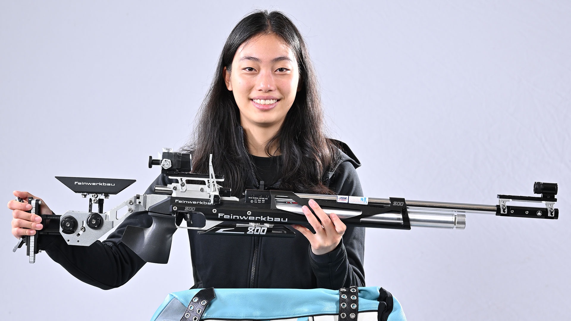 Eleanor Yang sitting in a chair while holding an air rifle