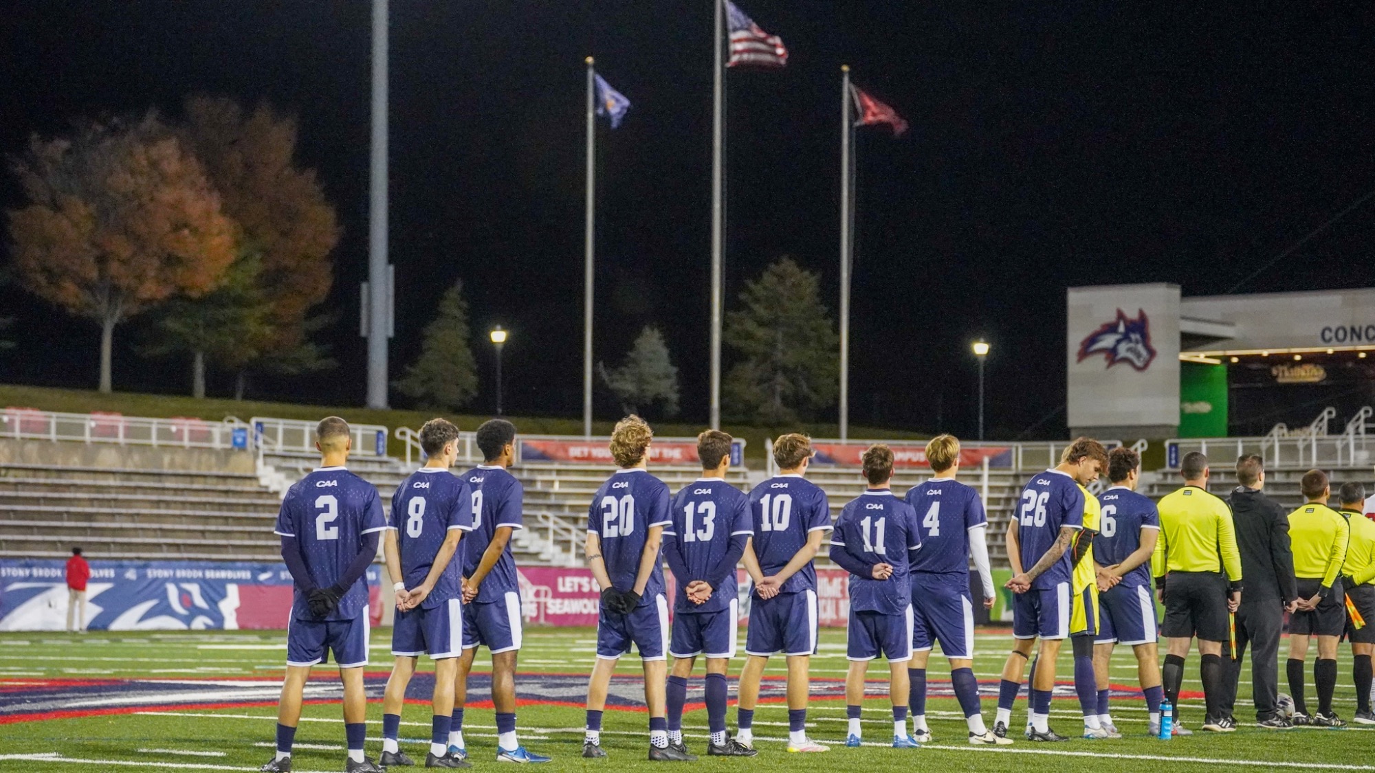 Men's Soccer stands with their backs to the camera in a line with the flags in the distance