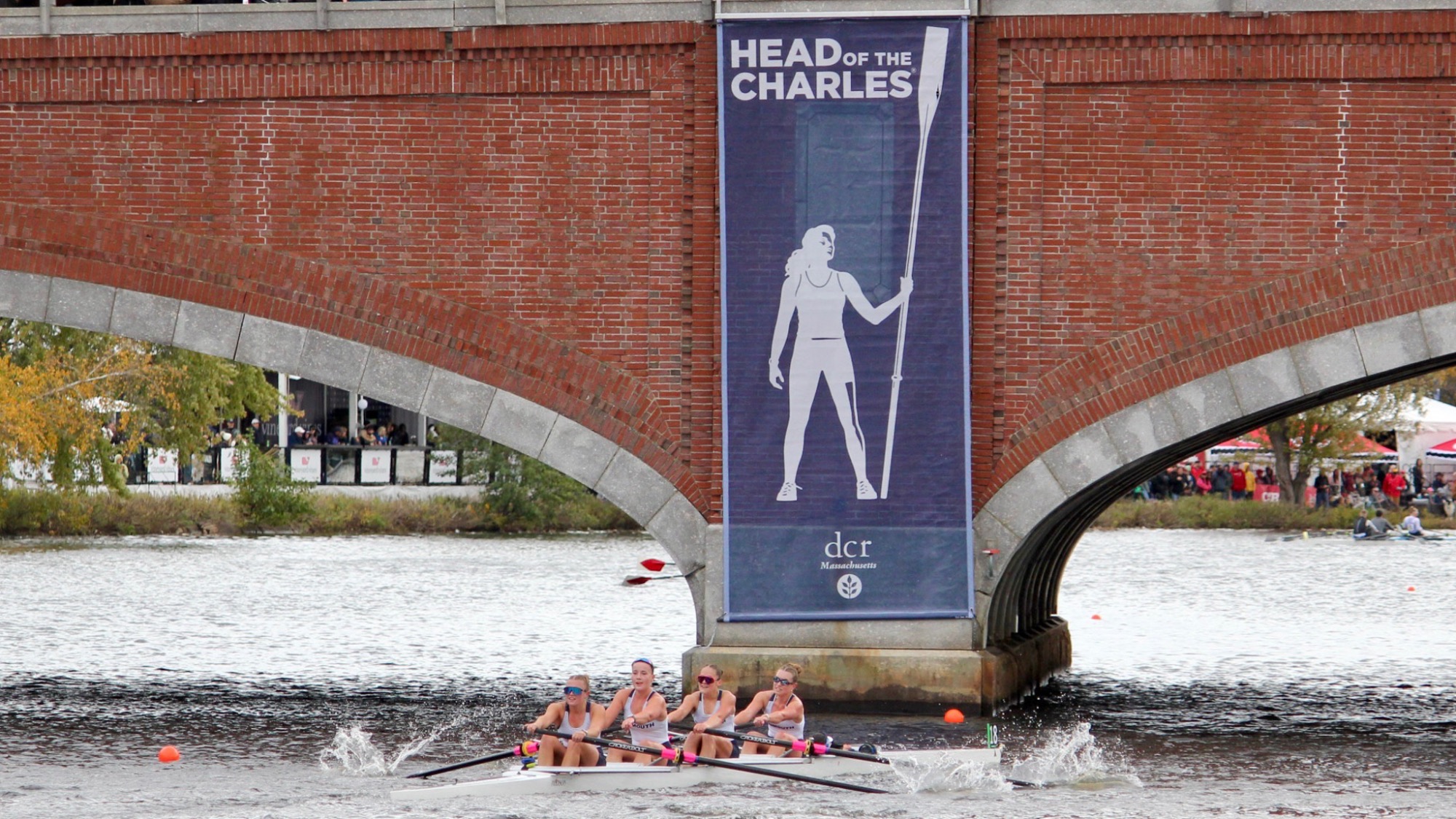 Monmouth 4+ boat rows towards the bridge where the Head of the Charles banner hangs