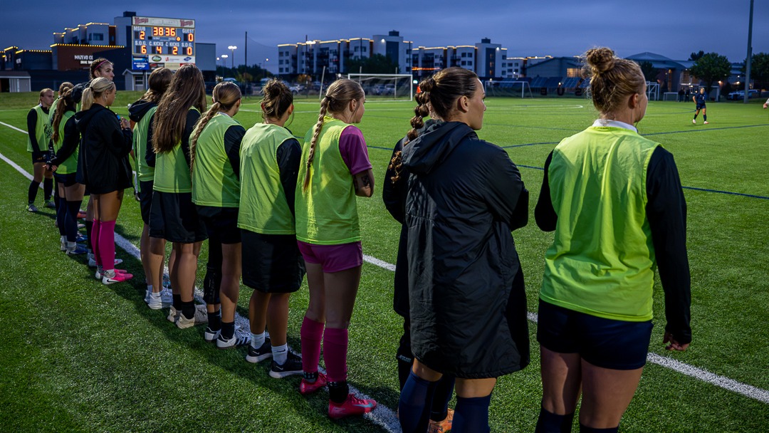 Members of the MSUB women's soccer team watch an ongoing match from the sidelines