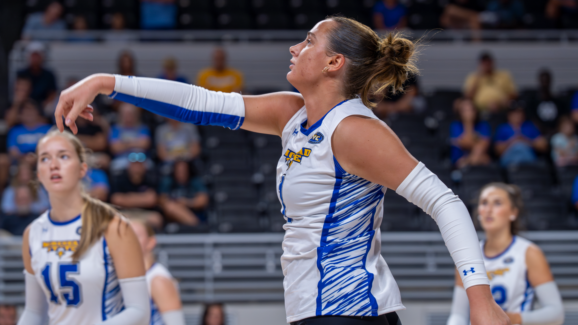  Brunette female in white volleyball jersey swings through a spike