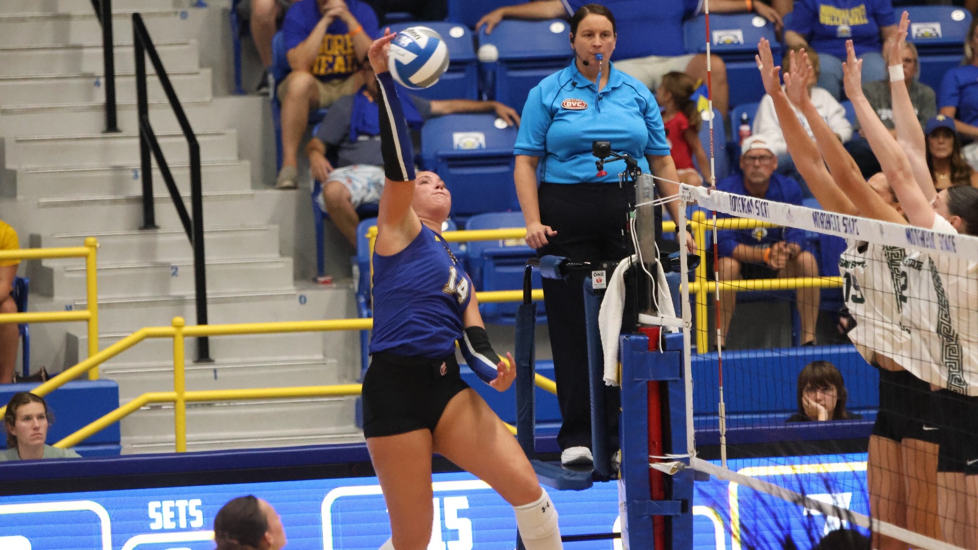 Blond girl in blue jersey hits a blue and white volleyball
