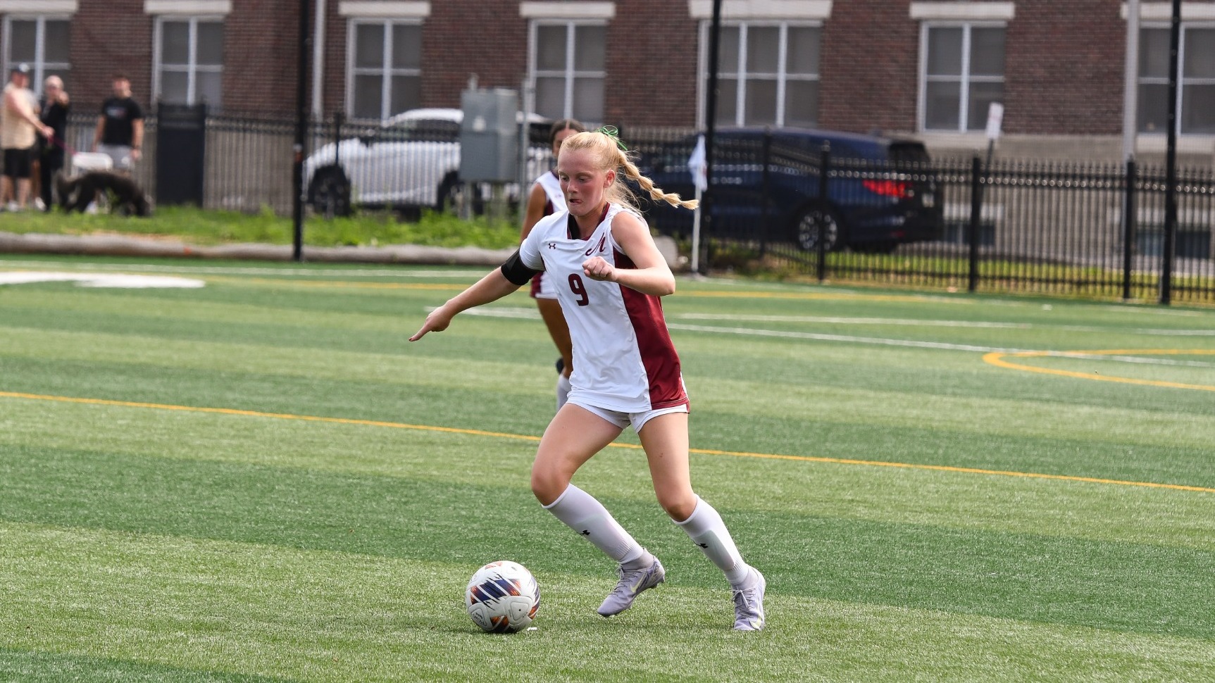 A soccer player in a white uniform dribbles the ball on a soccer field