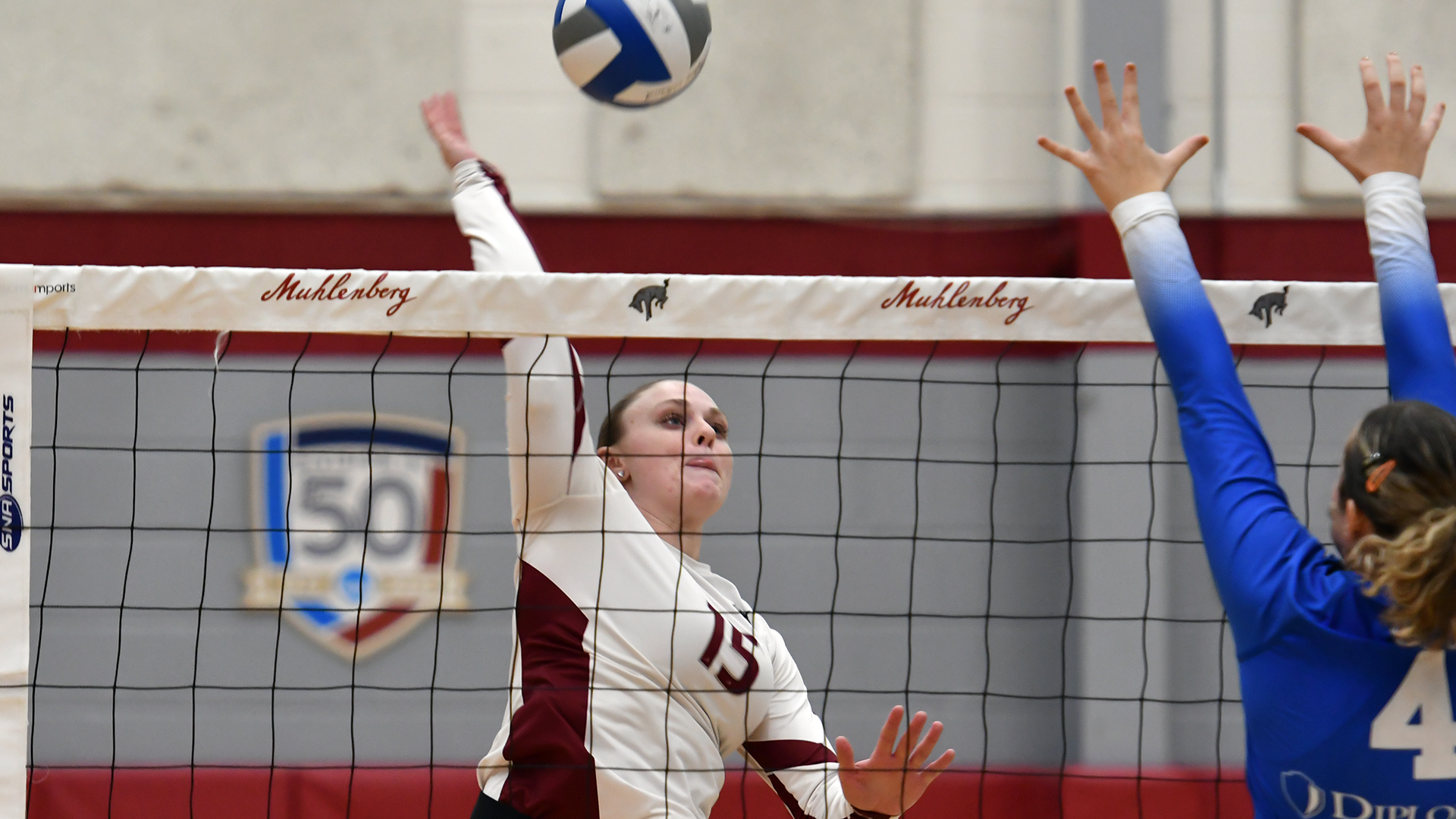 A volleyball player in a white jersey attacks the ball at the net