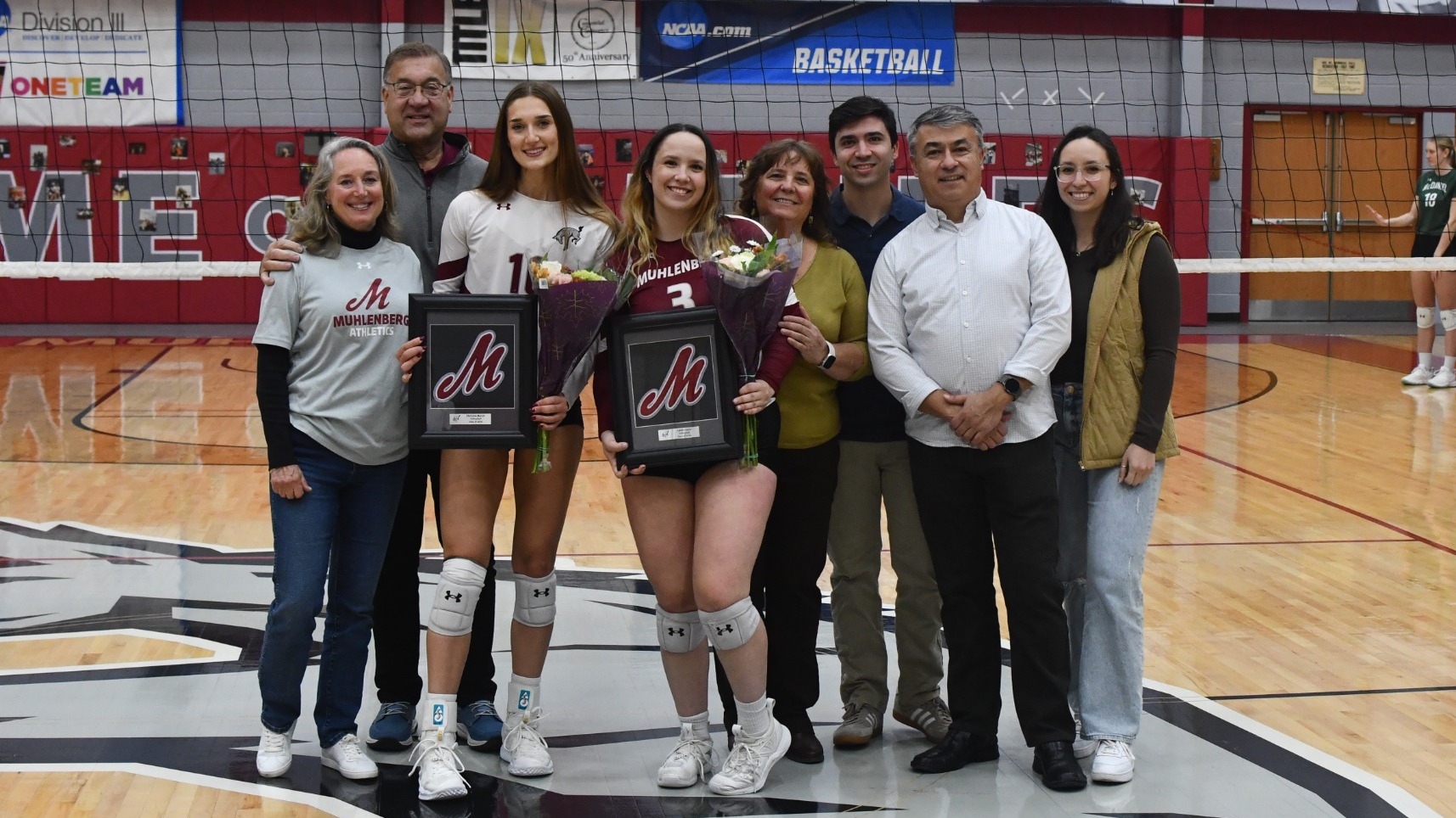 Two volleyball players stand with their respective families and pose for a photo