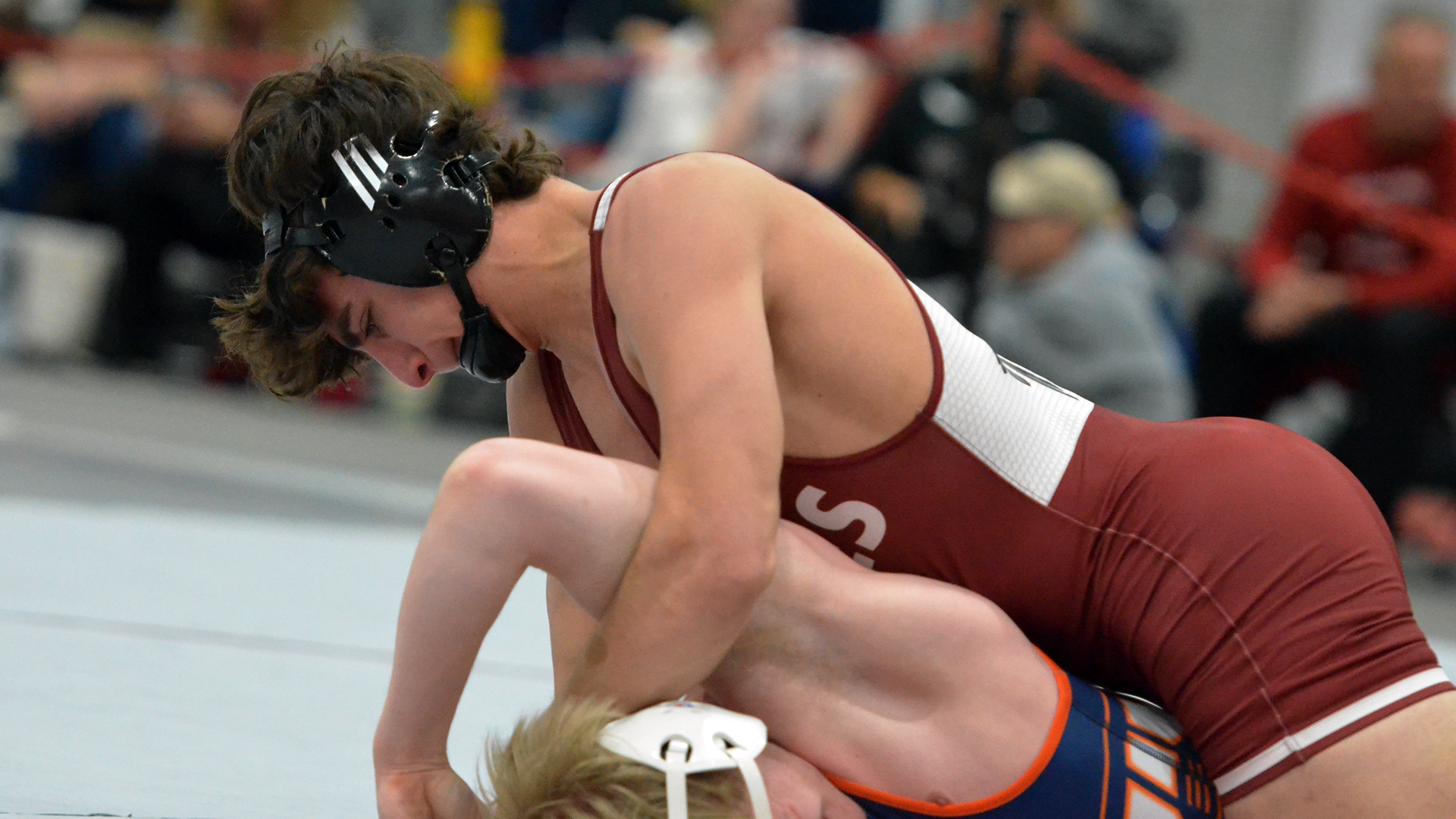 A wrestler in a red singlet on top of one in a blue singlet